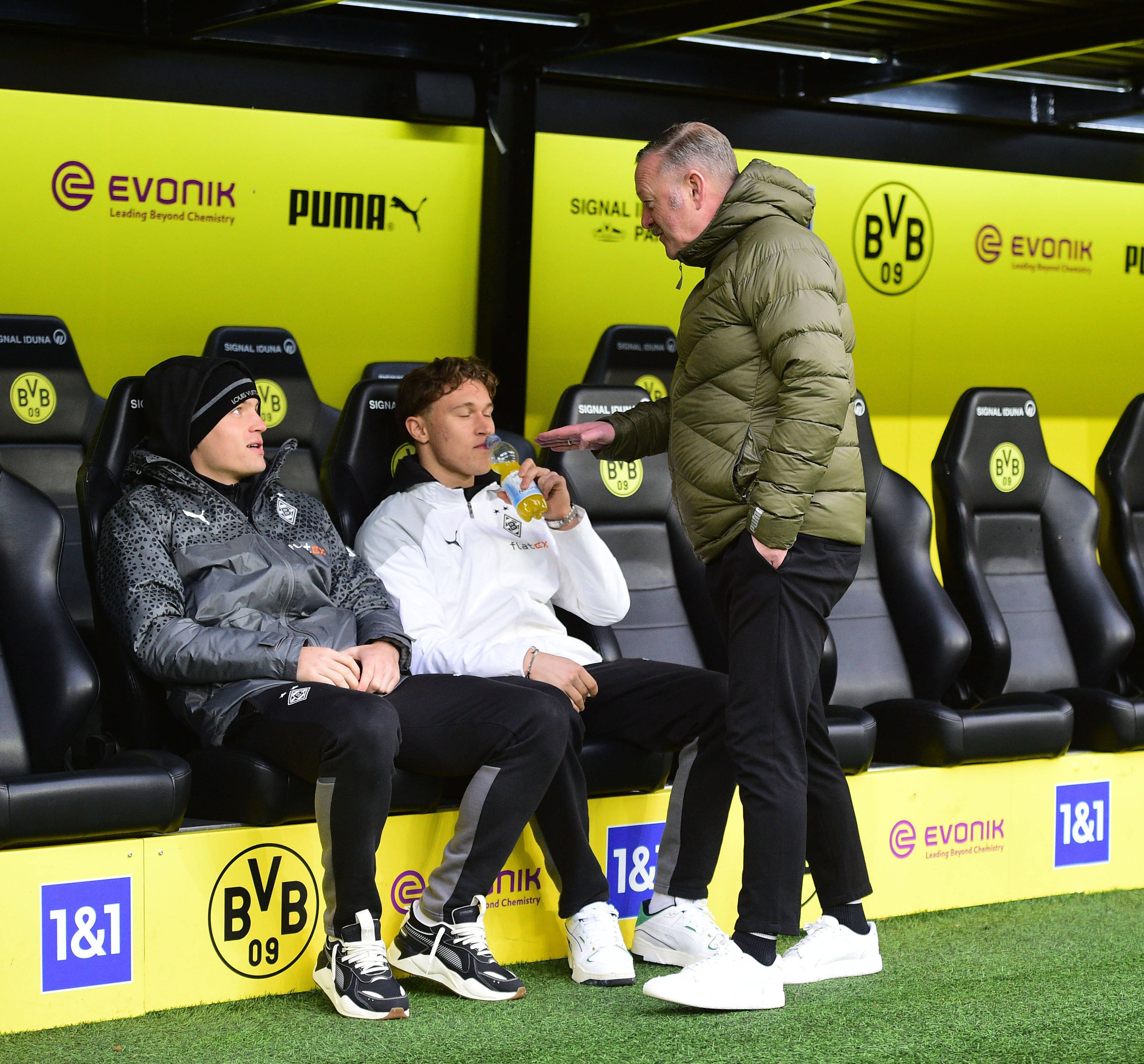 Roland Virkus redet lächelnd mit Luca Netz auf der Bank von Borussia Dortmund.
