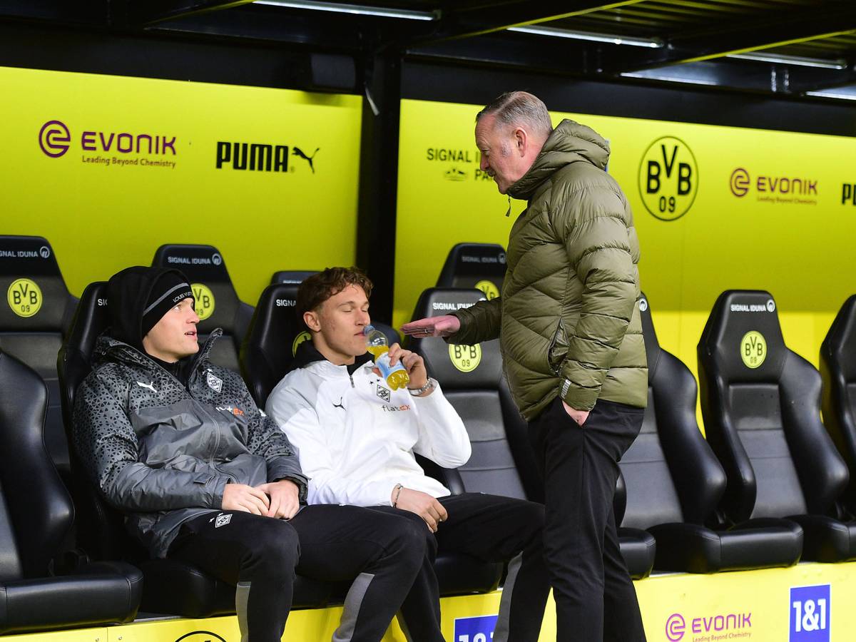 Roland Virkus redet lächelnd mit Luca Netz auf der Bank von Borussia Dortmund.
