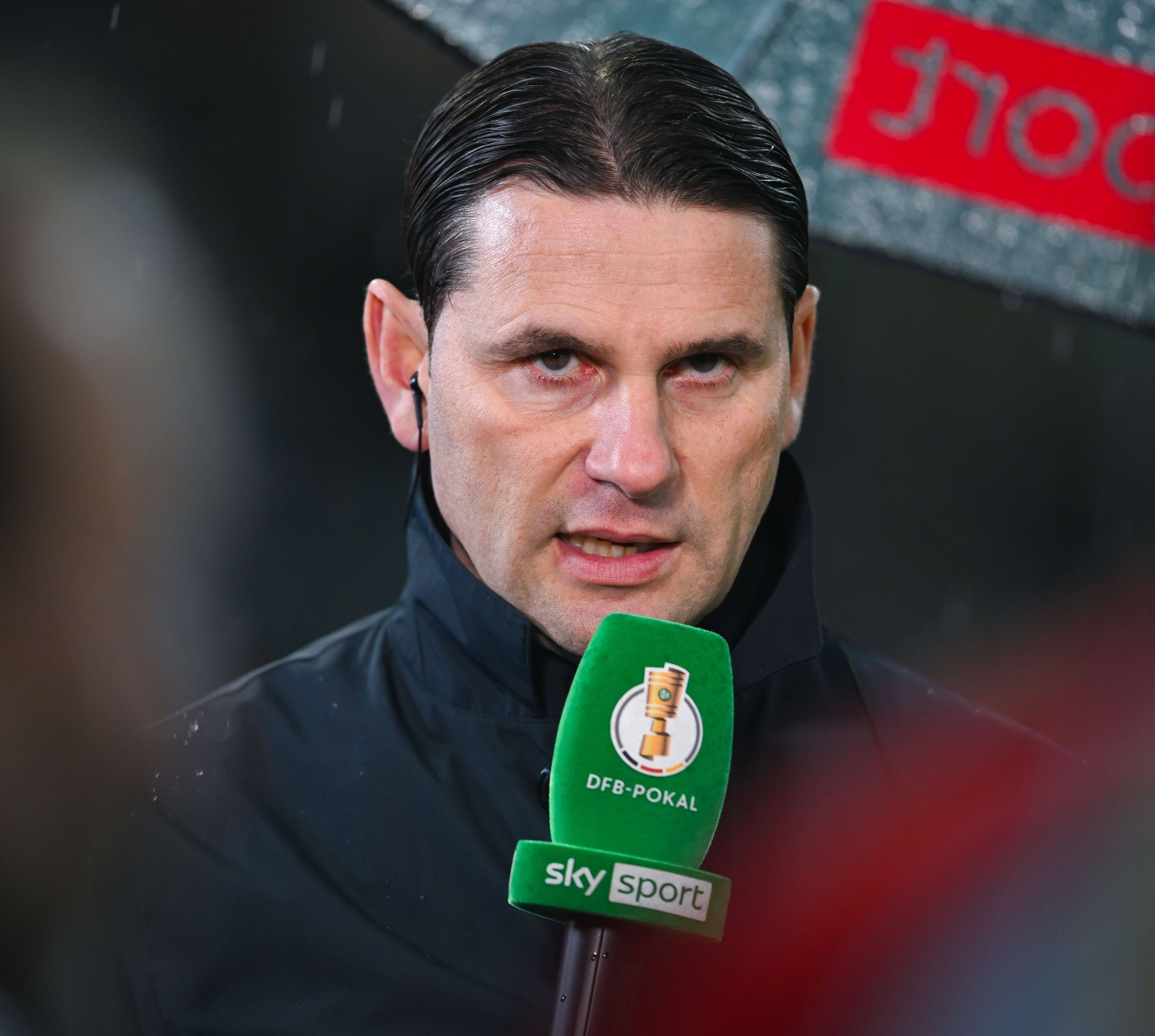 Trainer von Borussia Mönchengladbach spricht in ein Mikrofon.