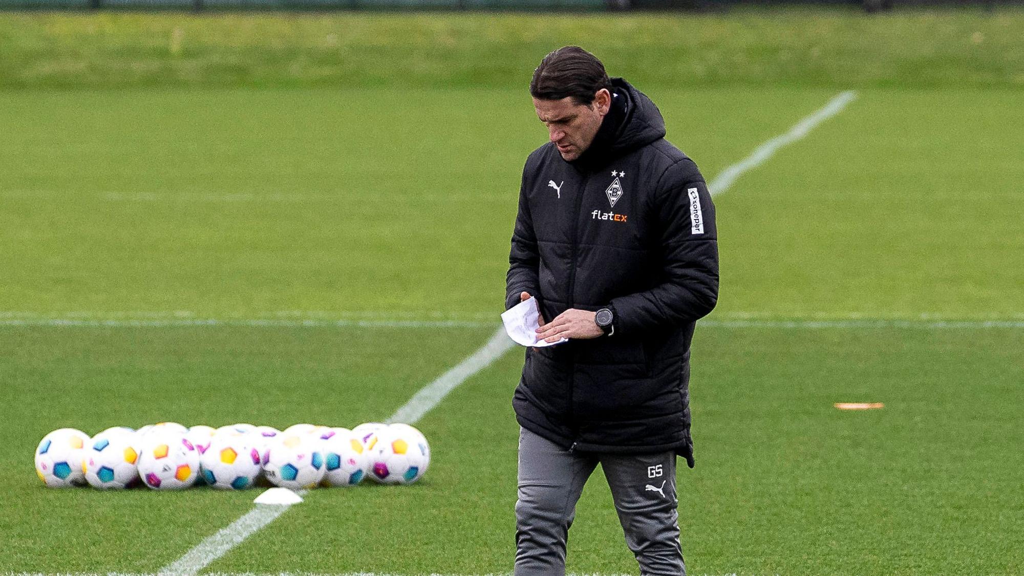 Trainer von Borussia Mönchengladbach während des Trainings mit einem Zettel in der Hand.