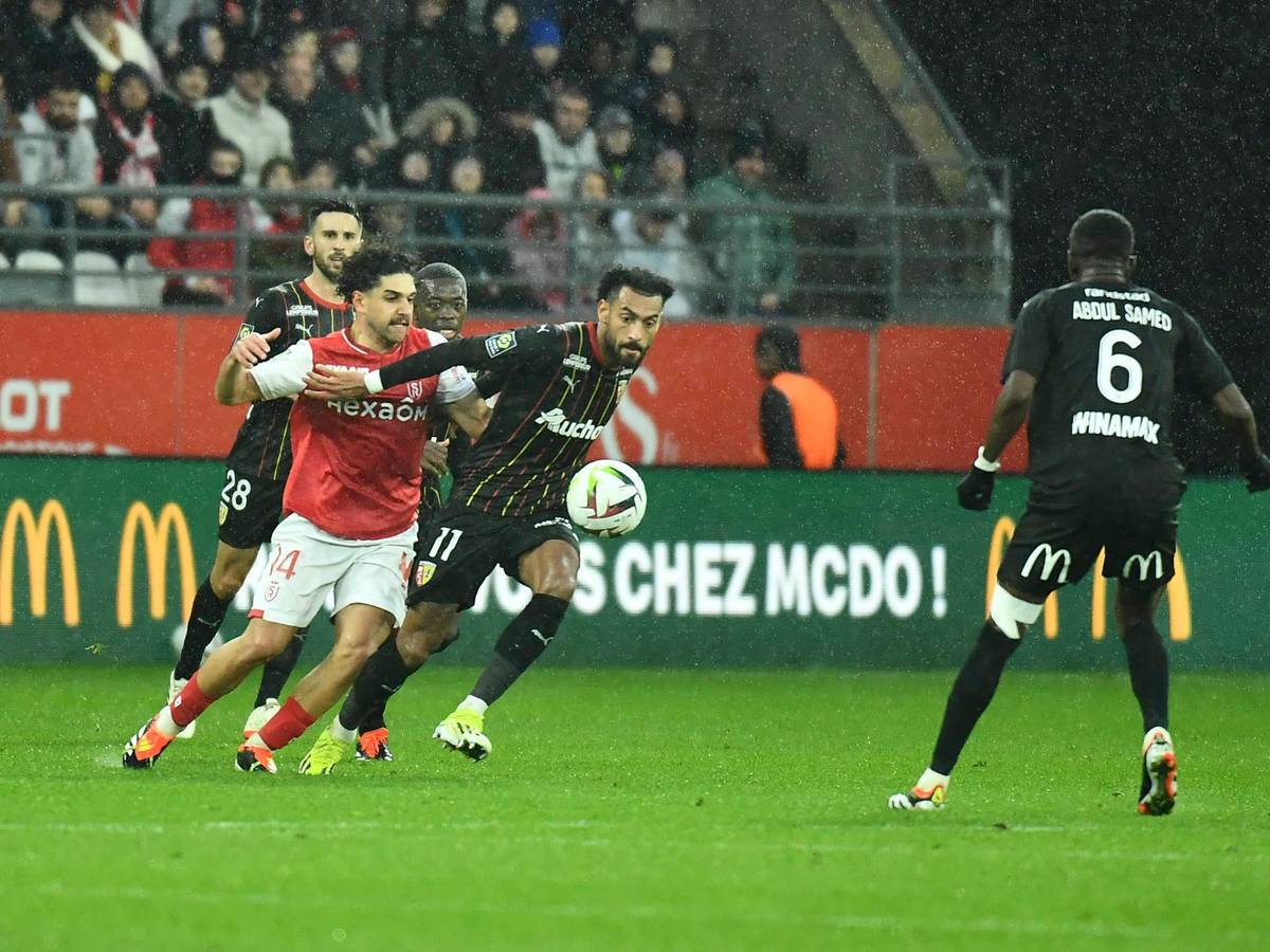 Reda Khadra im roten Reims-Trikot kämpft um den Ball mit Angelo Fulgini im schwarzen Lens-Trikot. Es regnet.