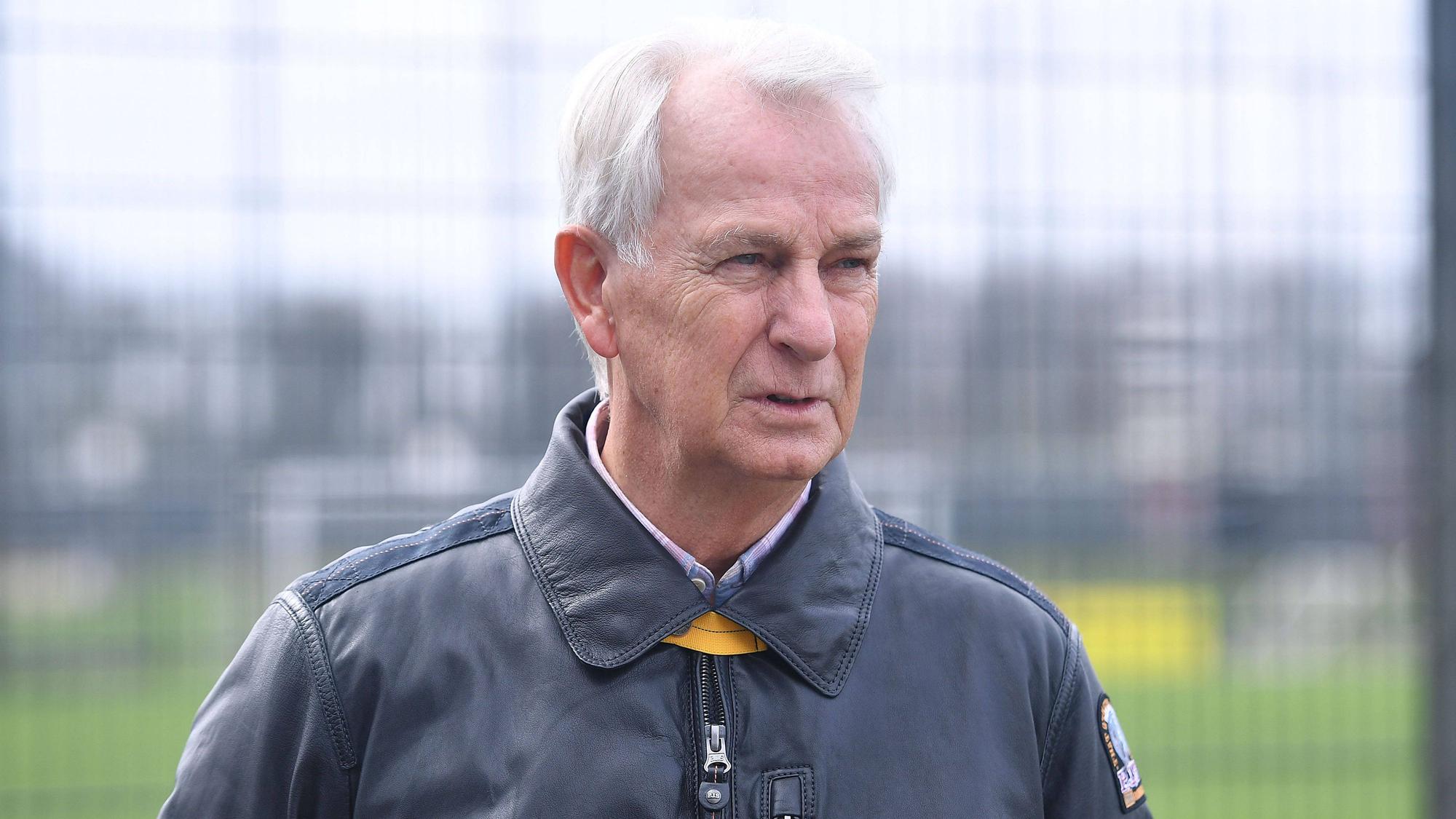 Rainer Bonhof mit fokussiertem Blick in einer Lederjacke am Trainingsplatz.