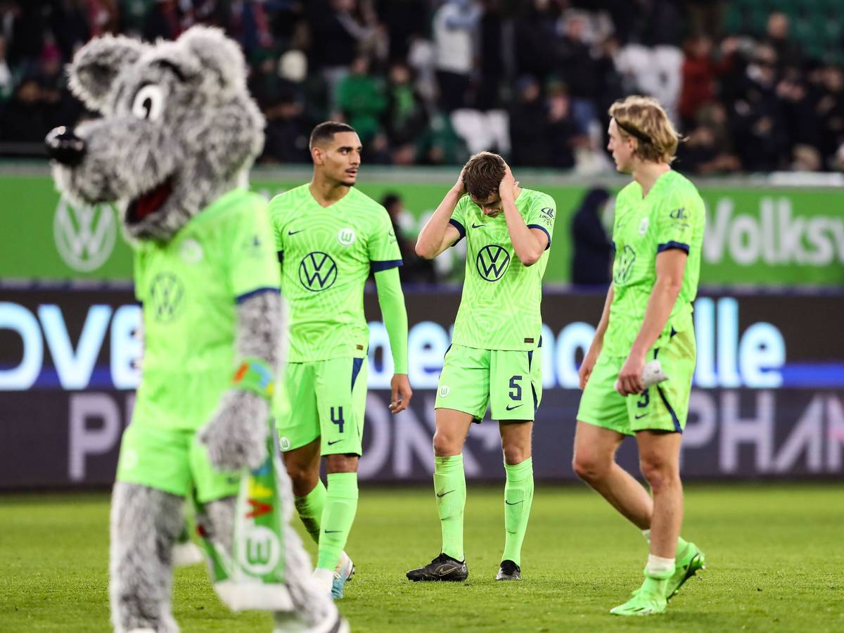 Drei Wolfsburg-Spieler ärgern sich. Auf der linken Seite läuft das Maskottchen Wölfi über den Platz.