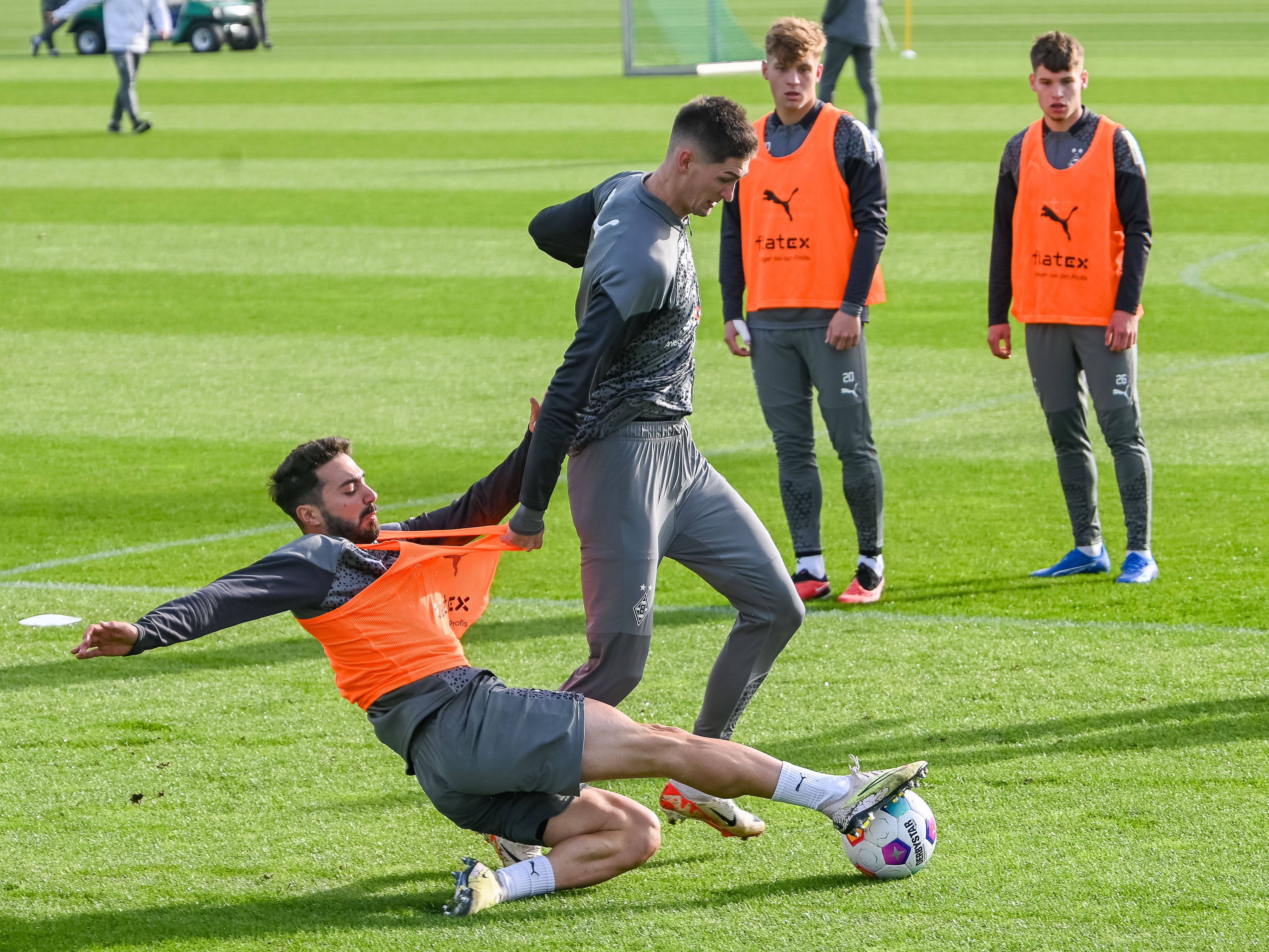 Lukas Ullrich und Luca Netz schauen zu, während sich Tomas Cvancara und Jacob Italiano im Borussia-Training duellieren.