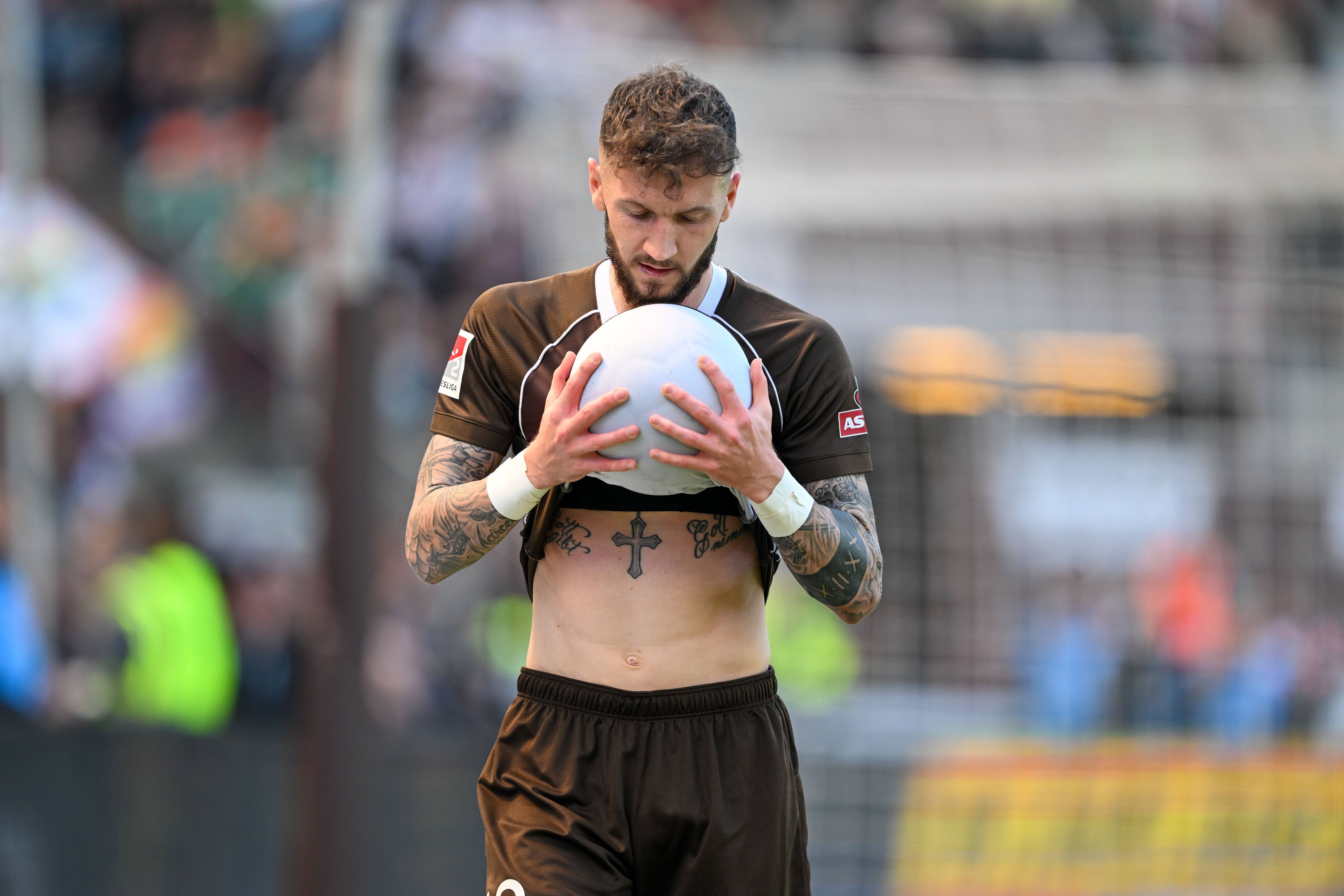 Marcel Hartel hält einen Ball mit beiden Händen fest.