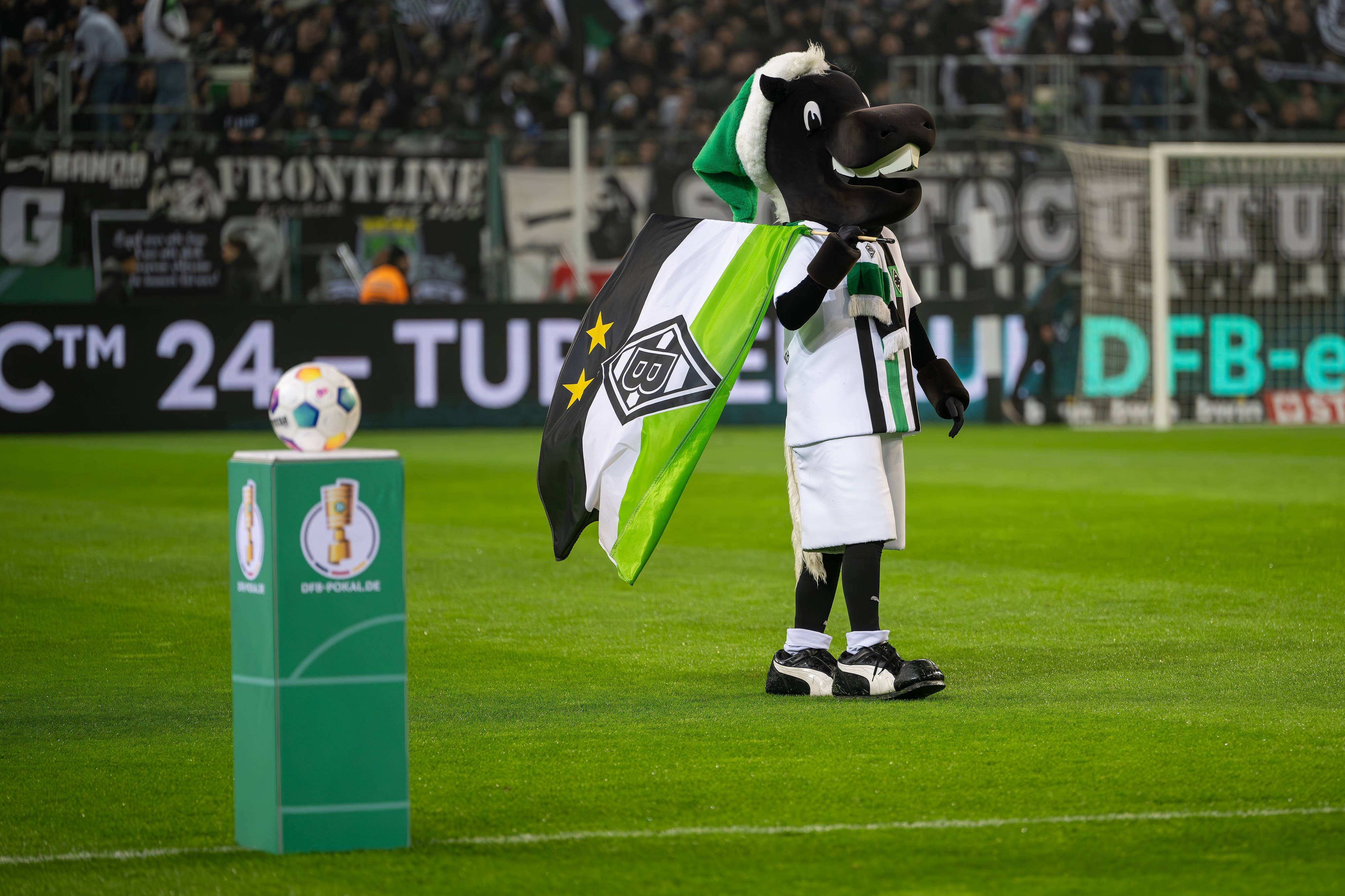 Maskottchen Jünter vor einem Sockel mit dem Pokal-Logo.