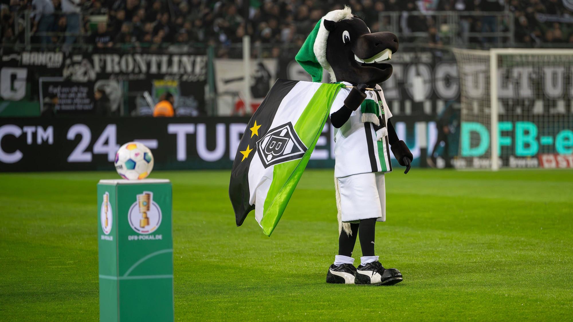 Maskottchen Jünter vor einem Sockel mit dem Pokal-Logo.