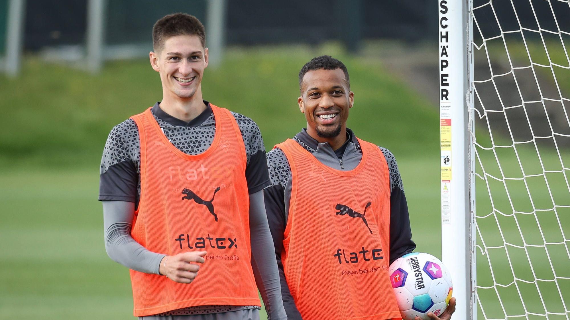 Die Gladbach-Profis Alassane Plea und Tomas Cvancara stehen lachend nebeneinander auf dem Trainingsplatz.