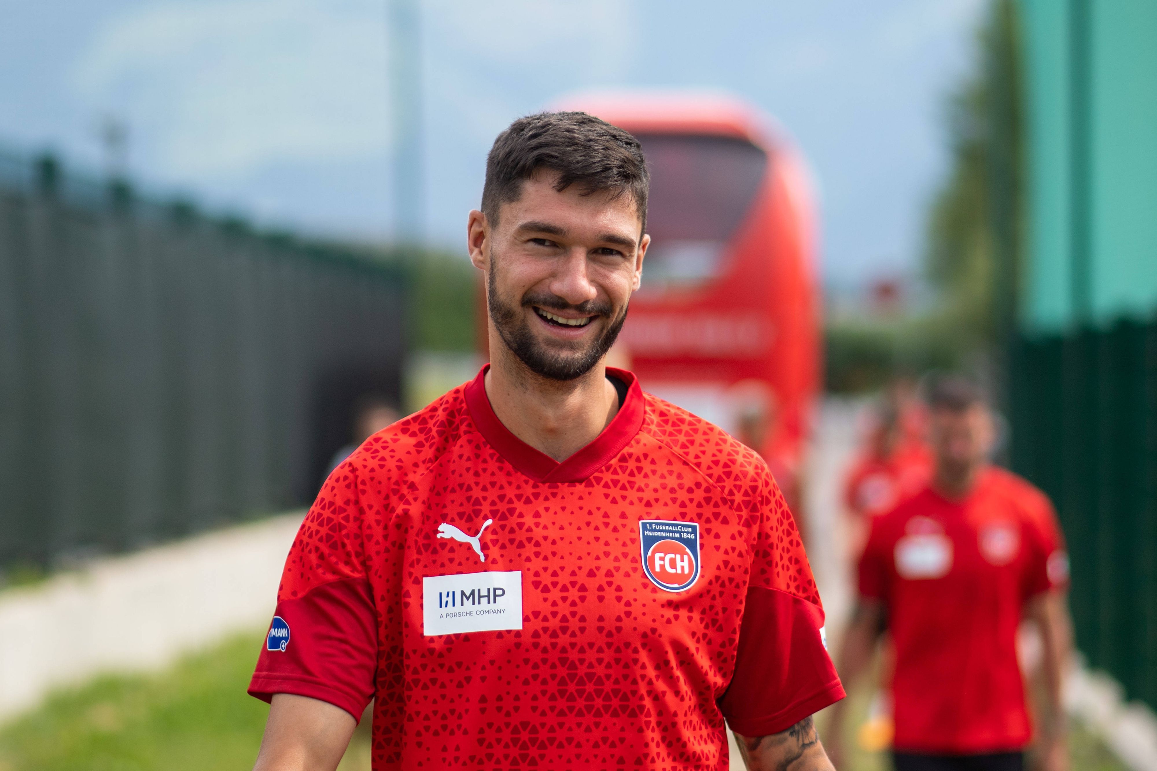 Heidenheims Stürmer Tim Kleindienst lächelt auf dem Weg zum Trainingsgelände in die Kamera.