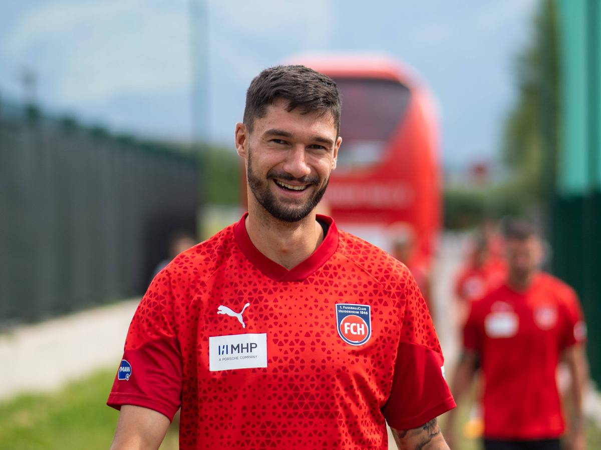 Heidenheims Stürmer Tim Kleindienst lächelt auf dem Weg zum Trainingsgelände in die Kamera.