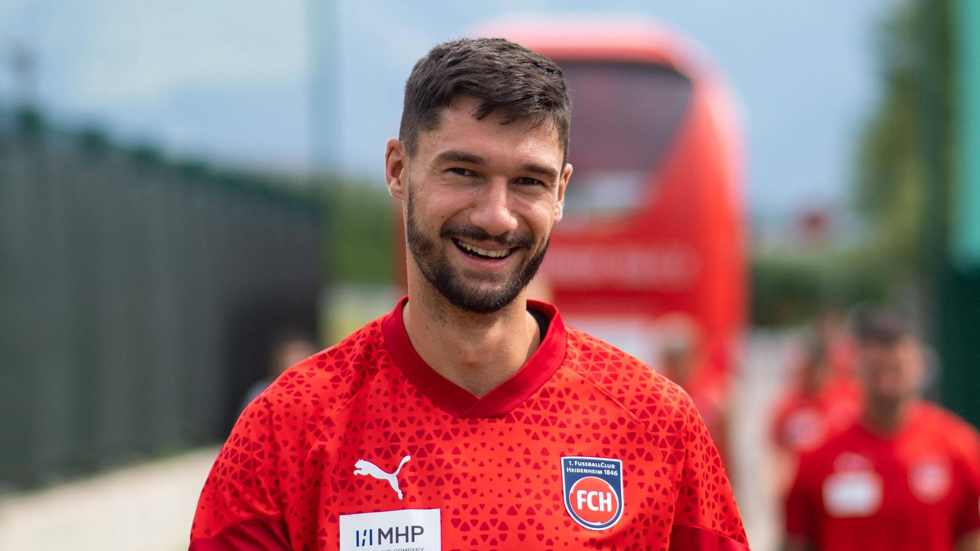 Heidenheims Stürmer Tim Kleindienst lächelt auf dem Weg zum Trainingsgelände in die Kamera.