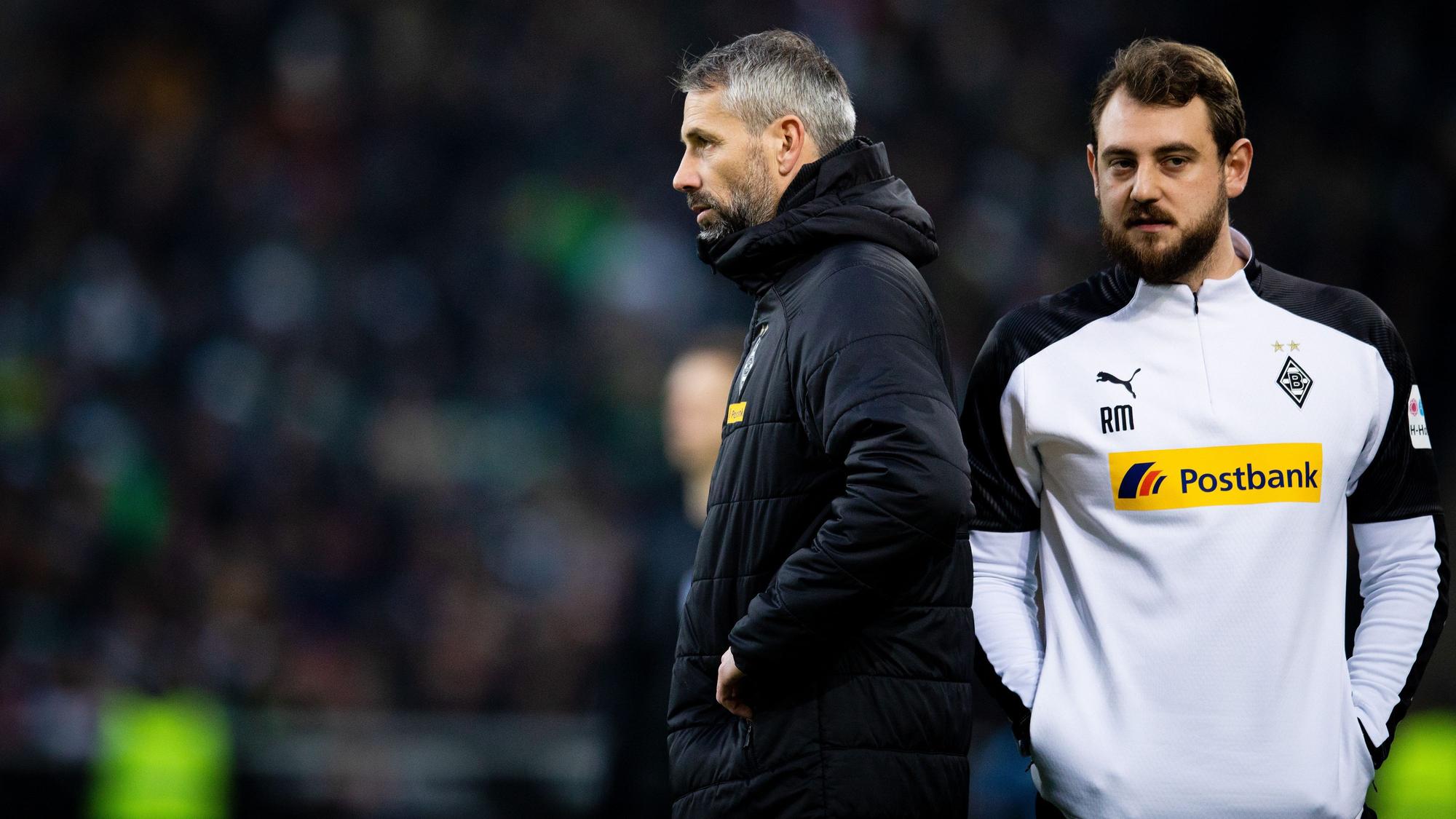 René Maric steht hinter Marco Rose in einer Gladbach-Jacke.