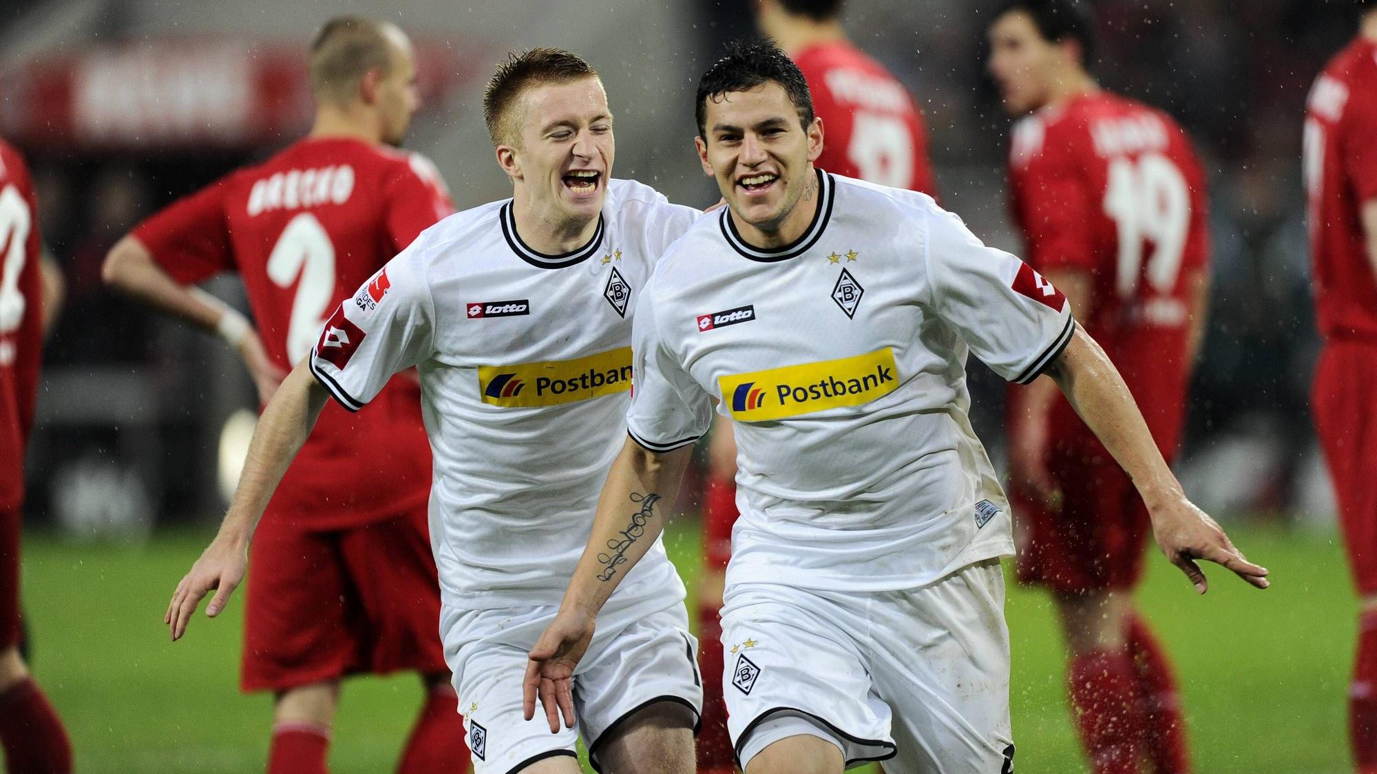 Raul Bobadilla und Marco Reus jubeln über ein Tor. Im Hintergrund sind enttäuschte Spieler des 1. FC Köln zu sehen.