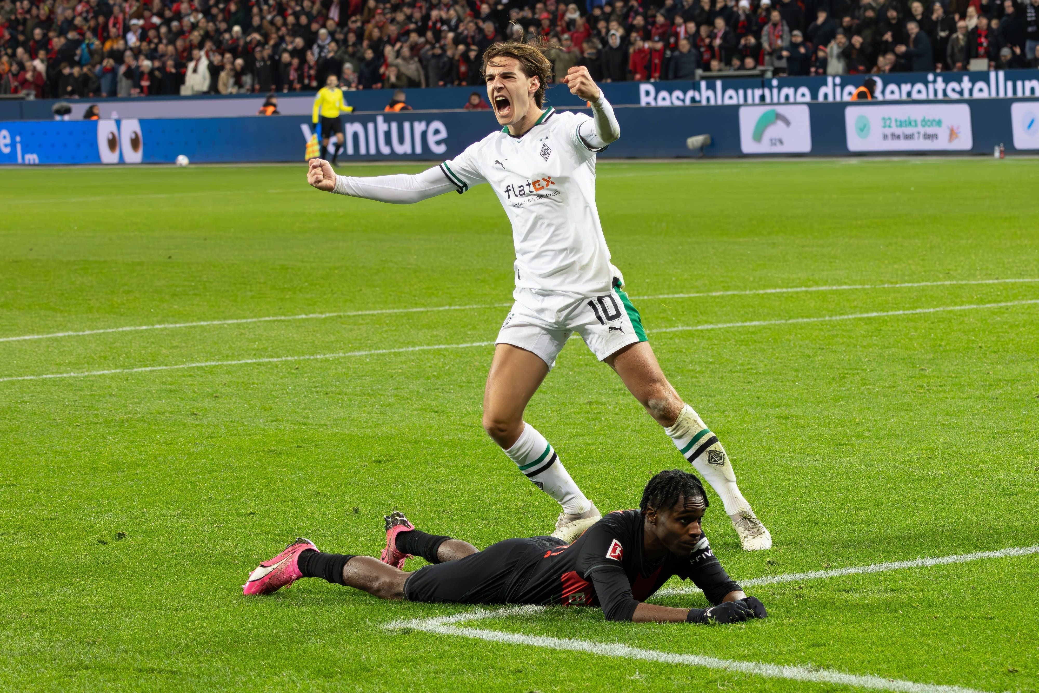 Florian Neuhaus bejubelt eine Grätsche gegen Jeremie Frimpong, der am Boden liegt.