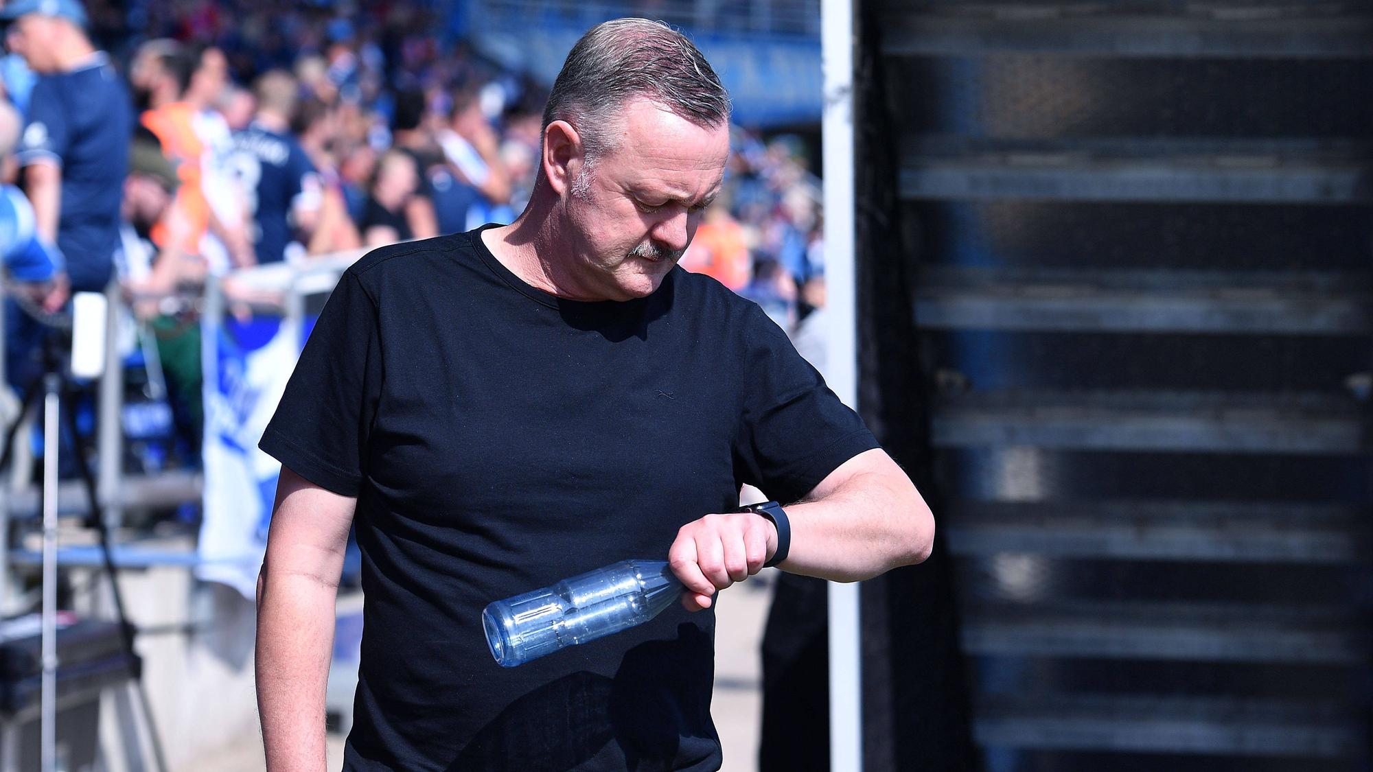 Roland Virkus schaut auf seine Armbanduhr und hält eine Wasserflasche in der Hand.