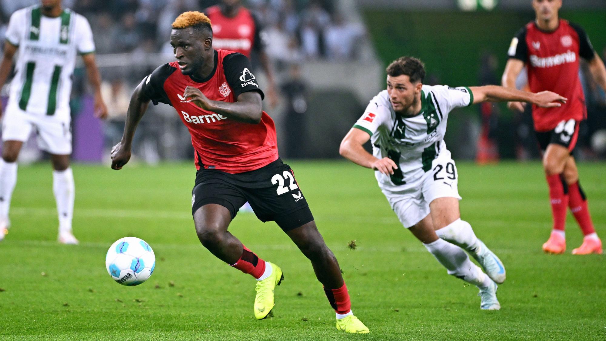 Bayer Leverkusens Victor Boniface führt den Ball, Borussia Mönchengladbachs Joe Scally verfolgt ihn.