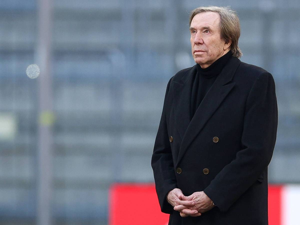 Günter Netzer steht in der Münchner Allianz-Arena auf dem Rasen und hat die Hände gefaltet.