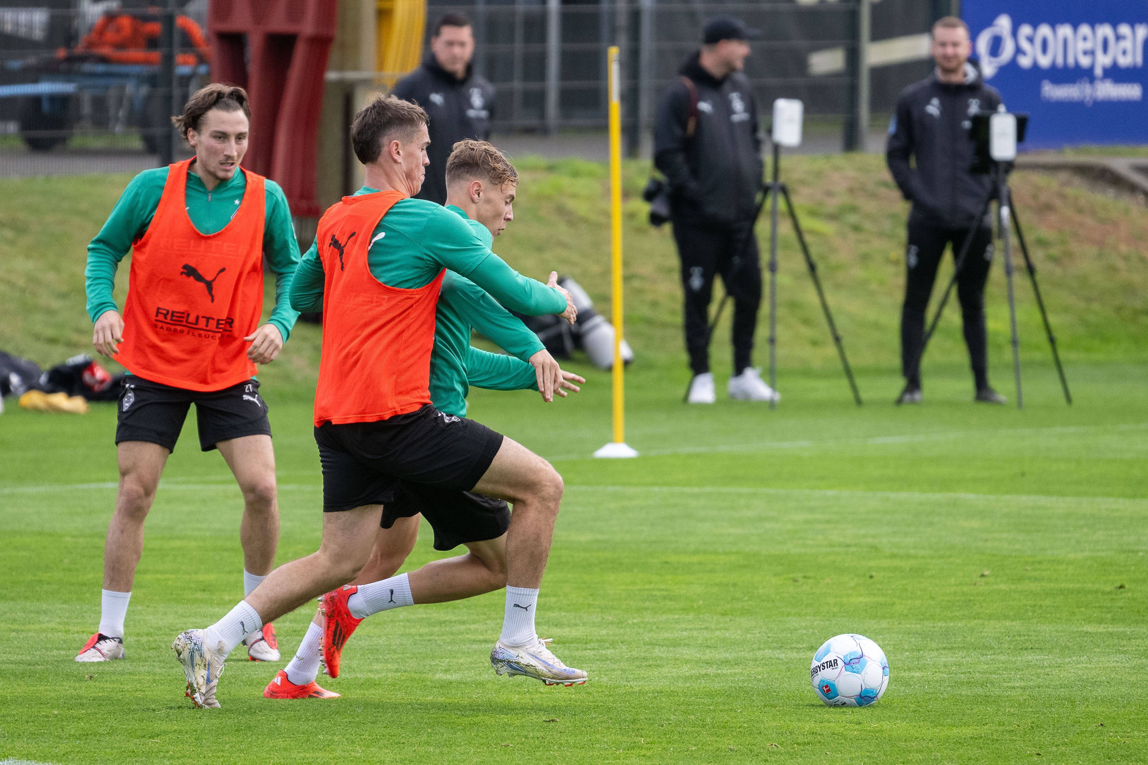 Borussia Mönchengladbachs Philipp Sander kämpft im Training mit Niklas Swider um den Ball. Im Hintergrund beobachtet Rocco Reitz die Szene.