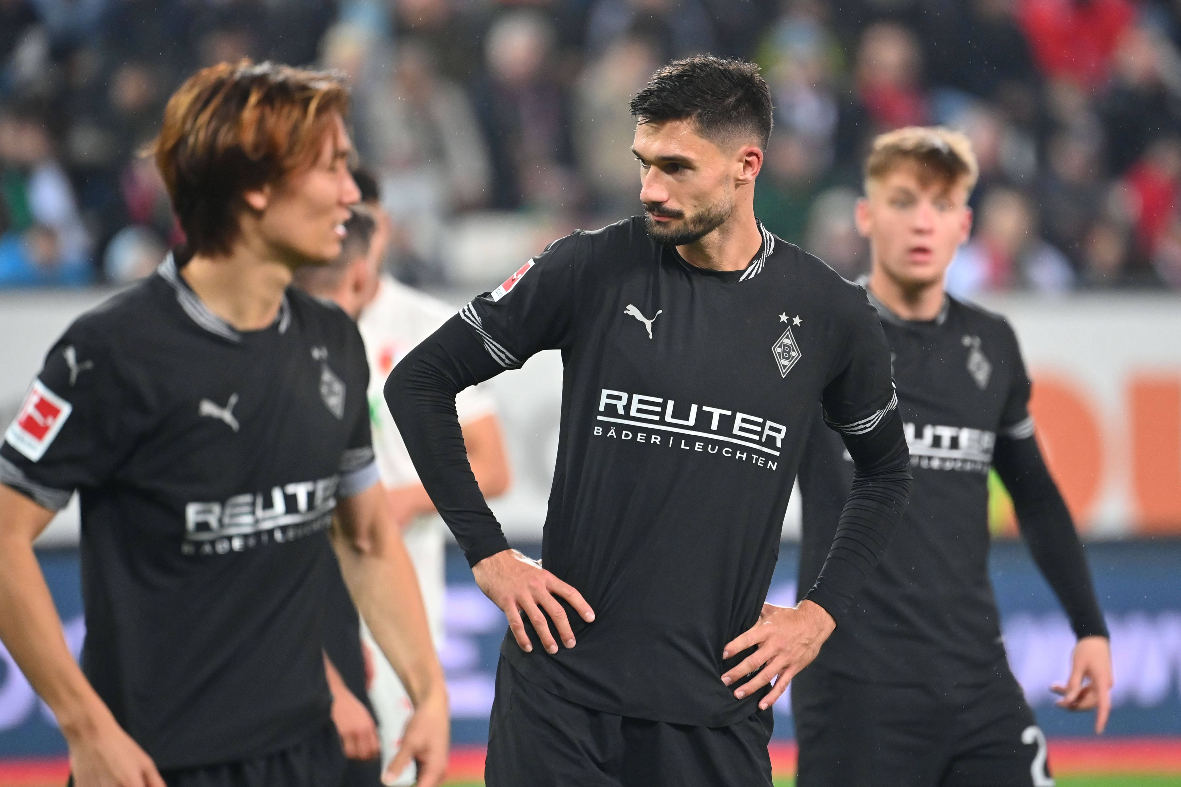 Die Gladbach-Profis Ko Itakura, Tim Kleindienst und Luca Netz stehen nach dem Spiel in Augsburg enttäuscht auf dem Rasen.