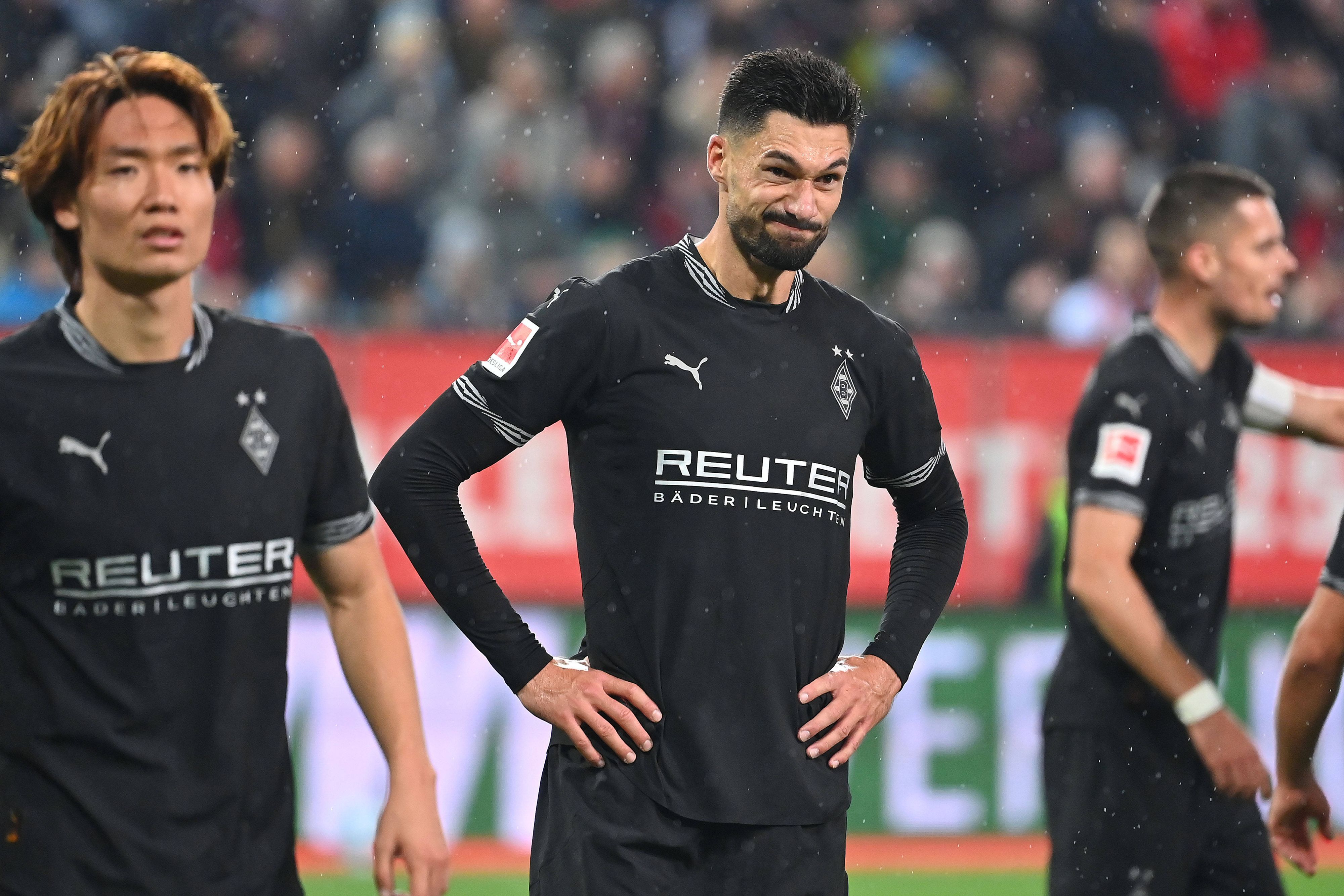 Borussia Mönchengladbachs Stürmer Tim Kleindienst steht nach dem Spiel beim FC Augsburg auf dem Rasen, hat die Arme in die Hüften gestemmt und verzieht das Gesicht.
