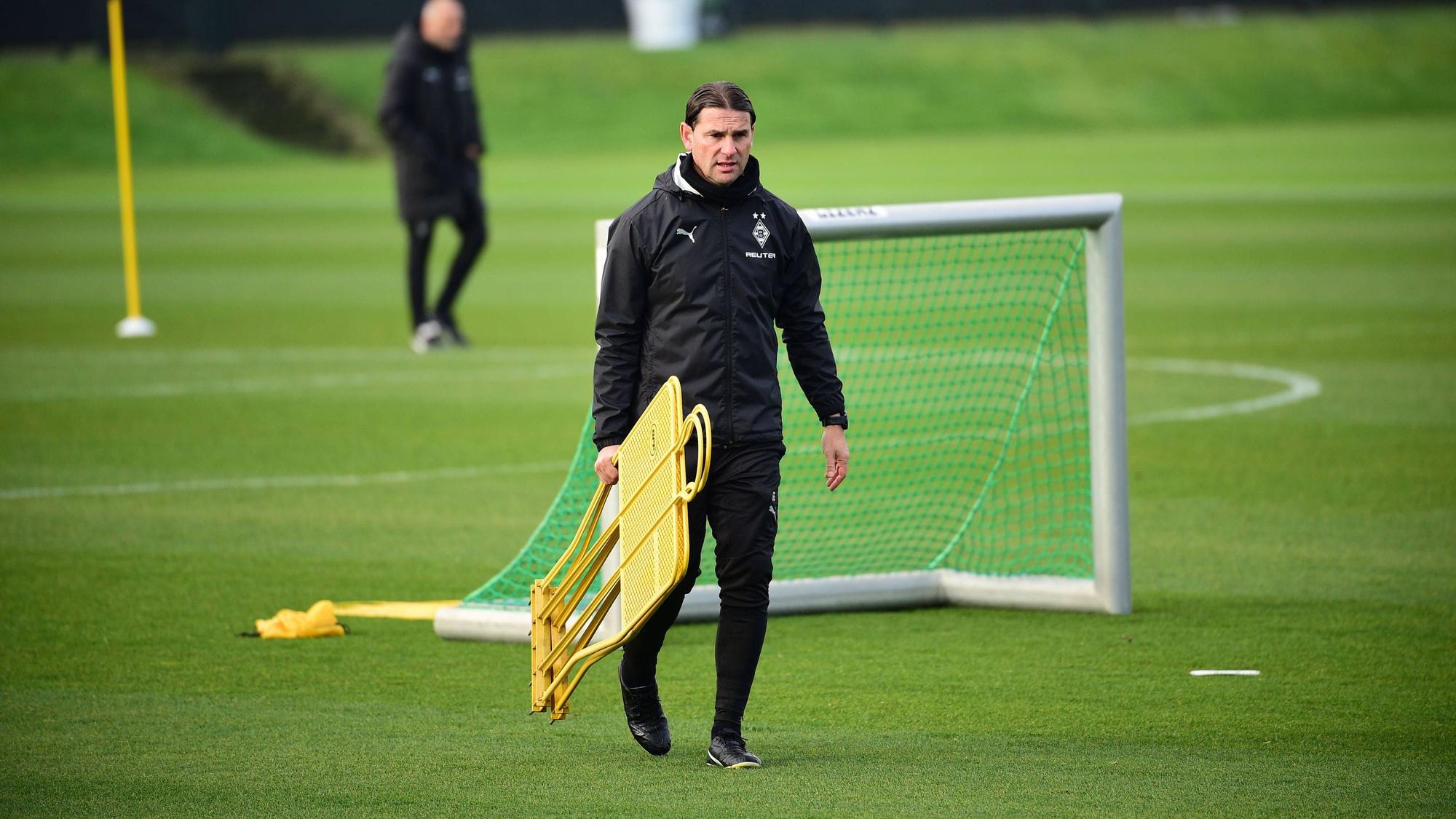 Borussia Mönchengladbachs Coach Gerardo Seoane läuft über den Trainingsplatz und trägt zwei Aufsteller in der rechten Hand.