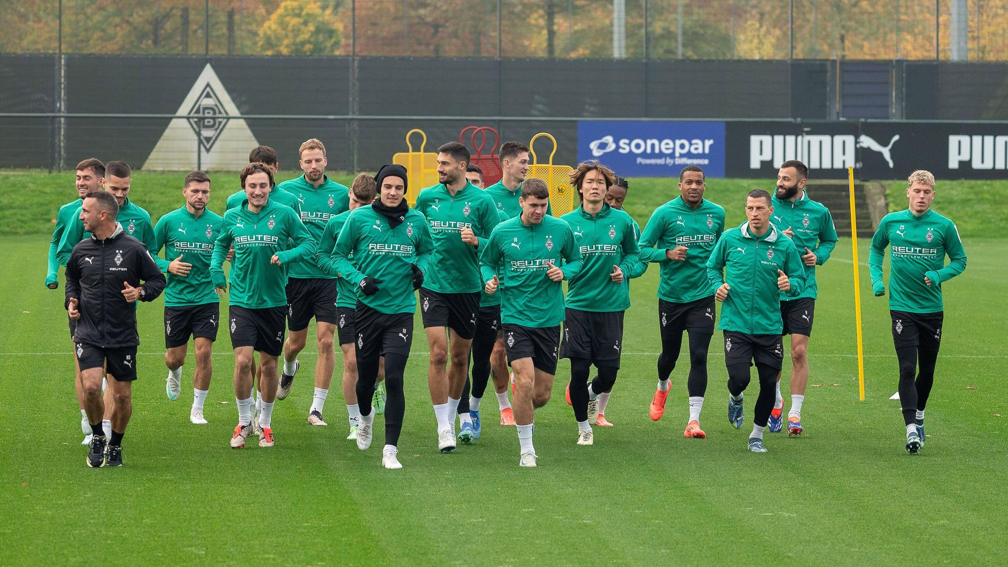 Die Spieler von Borussia Mönchengladbach laufen sich gemeinsam auf dem Trainingsplatz warm.