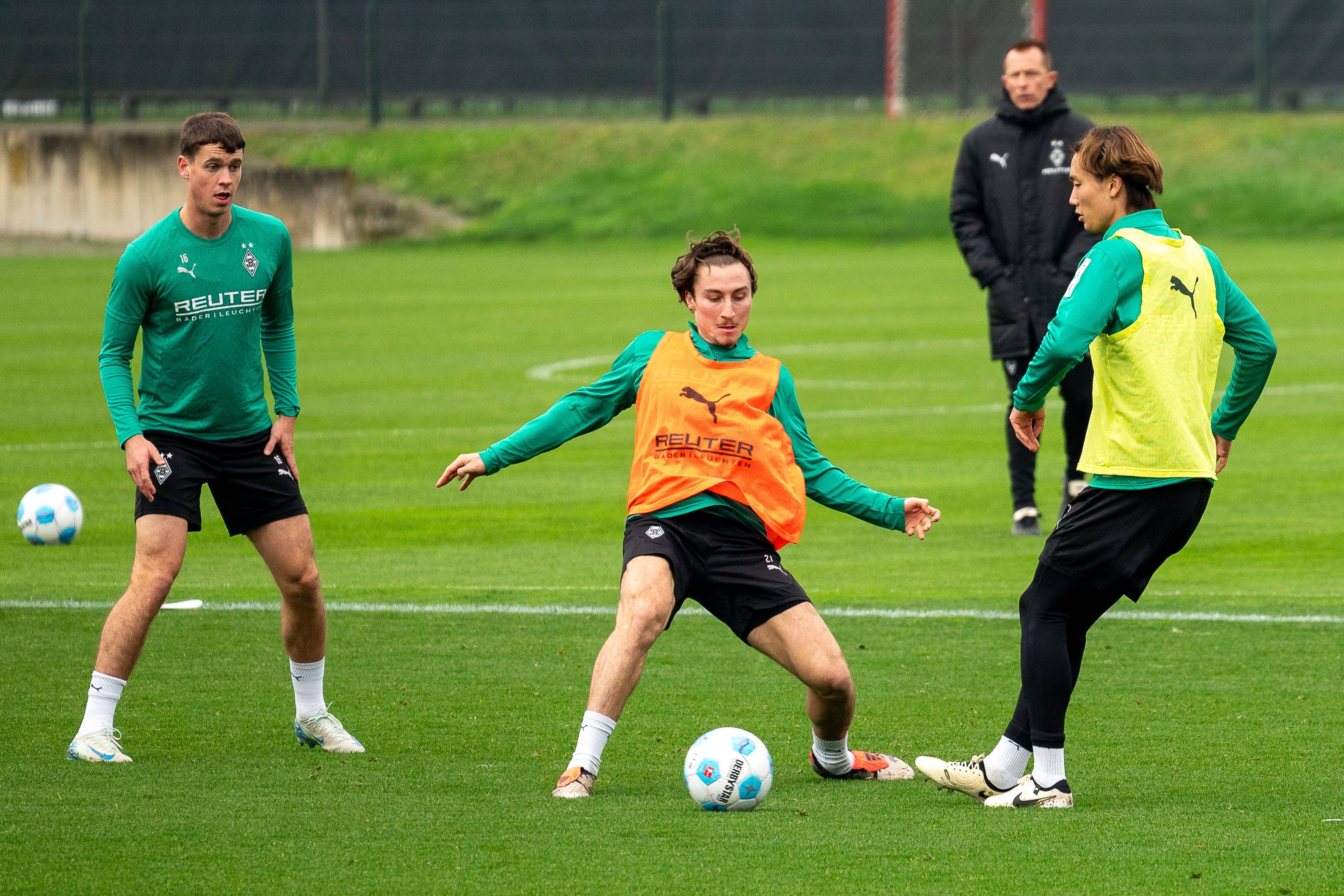 Die Gladbach-Profis Rocco Reitz und Ko Itakura kämpfen im Training um den Ball, links daneben beobachtet Philipp Sander die Szene.