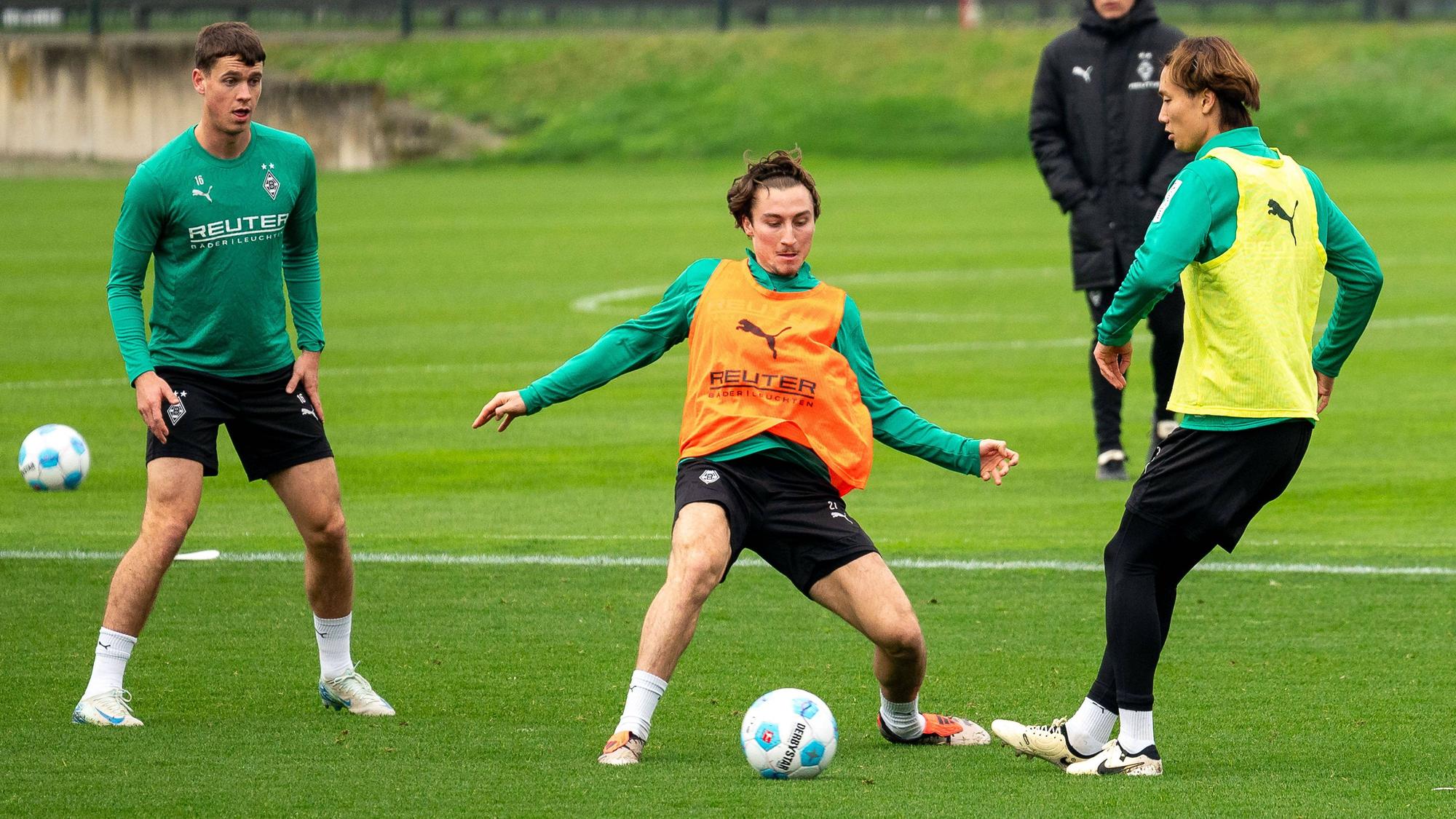 Die Gladbach-Profis Rocco Reitz und Ko Itakura kämpfen im Training um den Ball, links daneben beobachtet Philipp Sander die Szene.