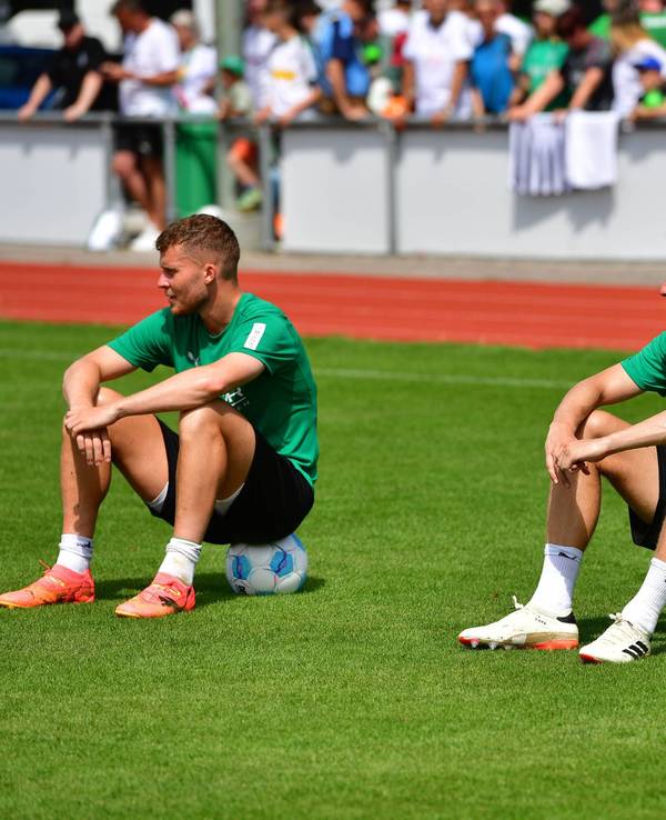 Die Gladbach-Profis Nico Elvedi und Marvin Friedrich und sitzen auf dem Trainingsplatz nebeneinander auf Fußbällen.
