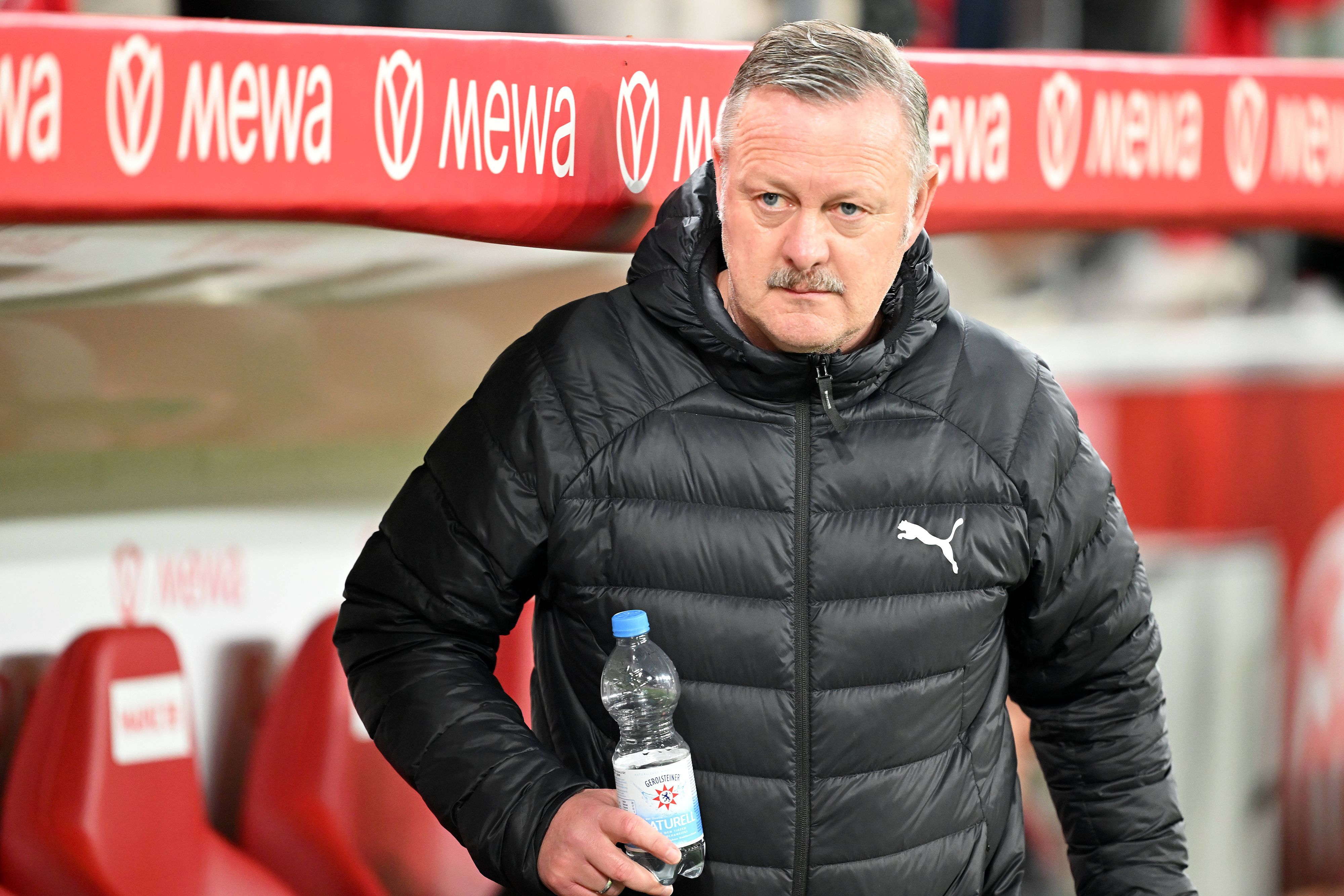 Roland Virkus beim Spiel in Mainz auf der Trainerbank mit einer Wasserflasche in der Hand.