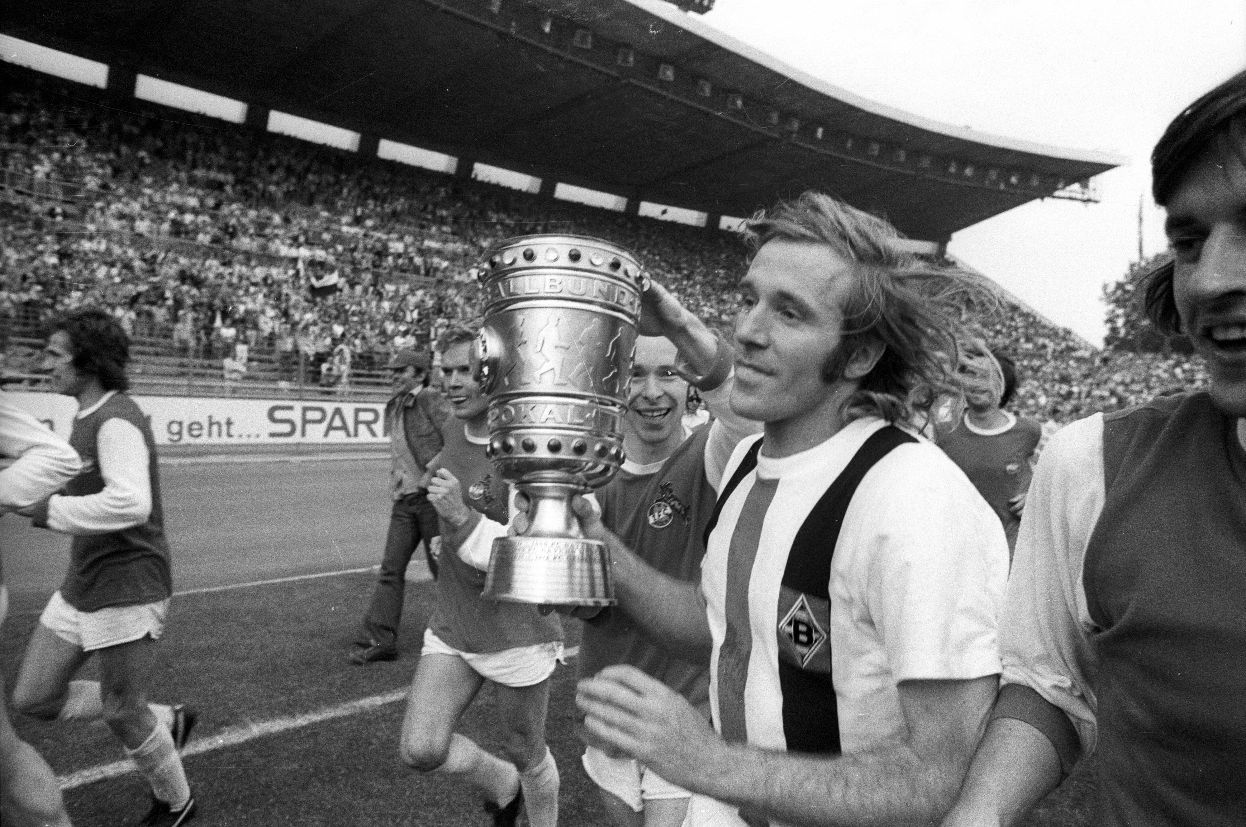 Günter Netzer hält den DFB-Pokal in den Händen auf dem Platz.