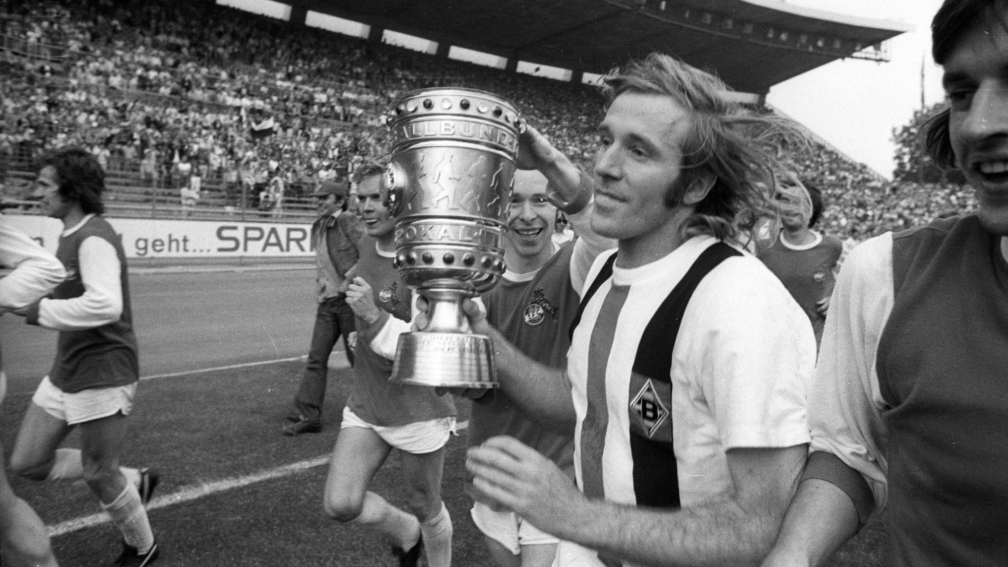 Günter Netzer hält den DFB-Pokal in den Händen auf dem Platz.