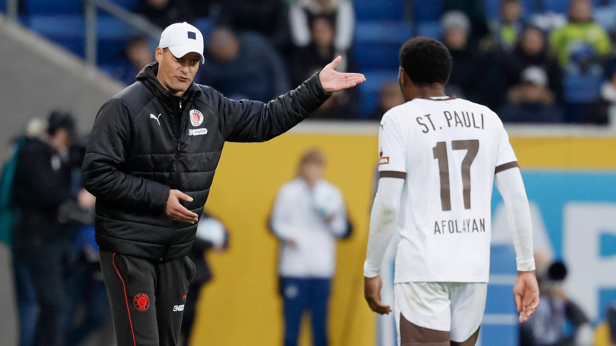 St. Paulis Trainer Alexander Blessin gibt seinem Stürmer Oladapo Afolayan im Spiel bei der TSG Hoffenheim an der Seitenlinie Anweisungen.