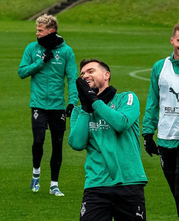 Borussia Mönchengladbachs Kevin Stöger steht lachend auf dem Trainingsplatz, dahinter steht Teamkollege Nico Elvedi und lächelt ebenfalls.