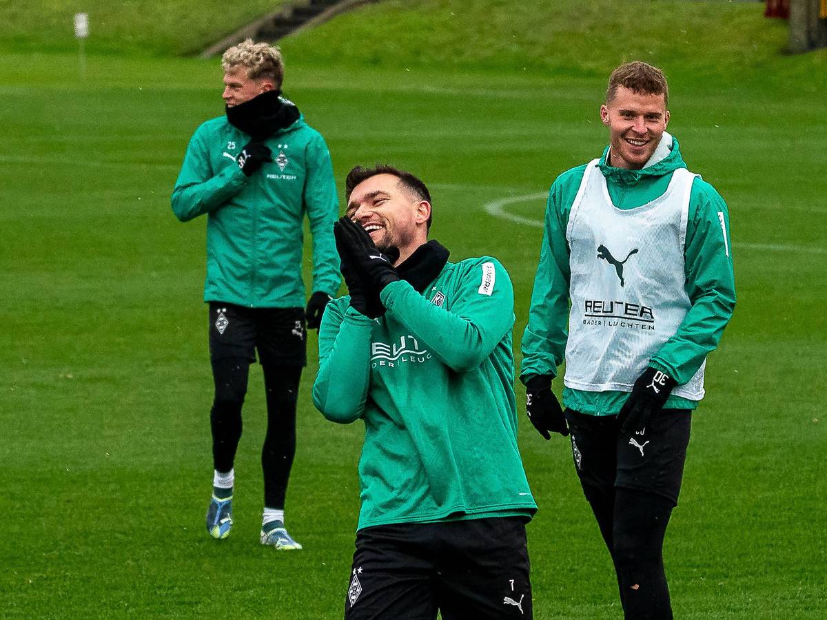 Borussia Mönchengladbachs Kevin Stöger steht lachend auf dem Trainingsplatz, dahinter steht Teamkollege Nico Elvedi und lächelt ebenfalls.
