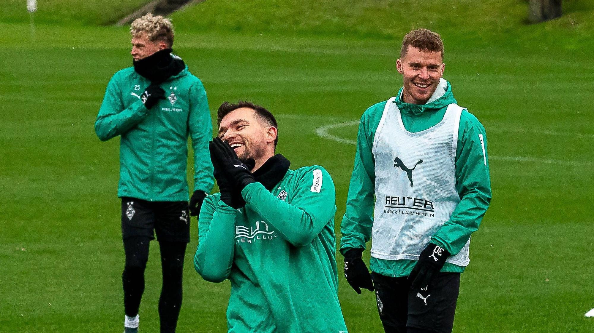 Borussia Mönchengladbachs Kevin Stöger steht lachend auf dem Trainingsplatz, dahinter steht Teamkollege Nico Elvedi und lächelt ebenfalls.