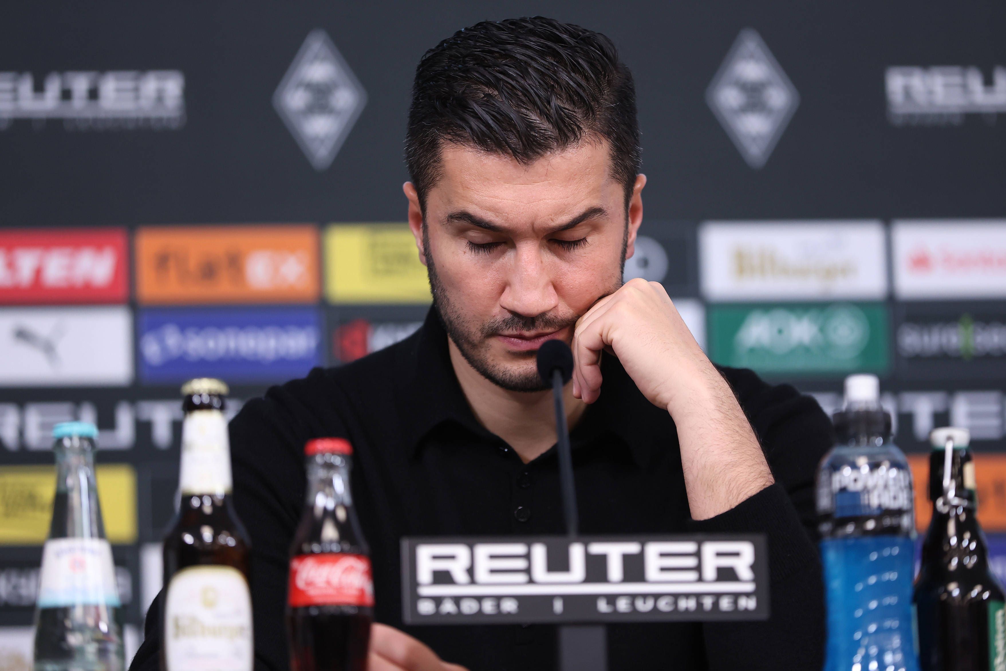 Borussia Dortmunds Trainer Nuri Sahin sitzt bei der Pressekonferenz nach dem Spiel bei Borussia Mönchengladbach auf dem Podium und stützt den Kopf auf seine linke Hand.