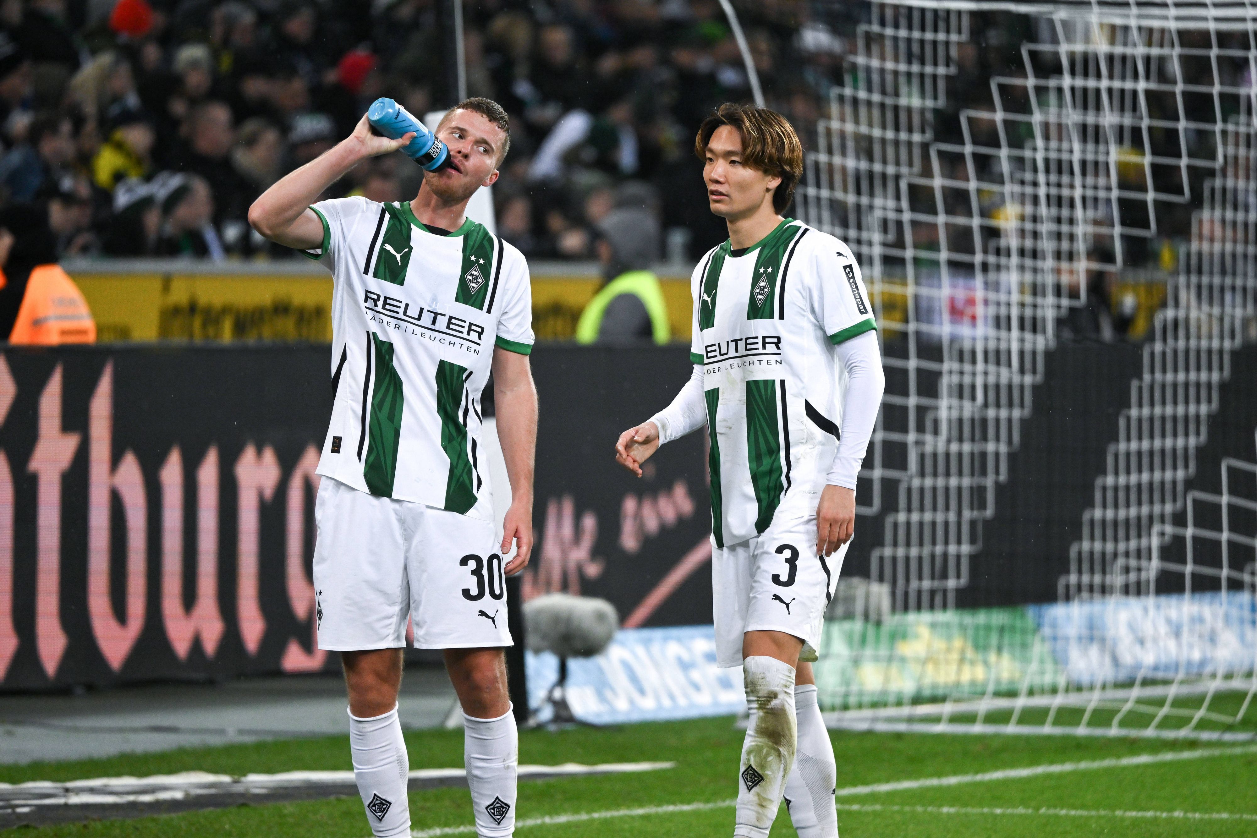 Die Gladbach-Profis Nico Elvedi und Ko Itakura stehen beim Spiel gegen Borussia Dortmund nebeneinander, Elvedi trinkt aus einer Wasserflasche.