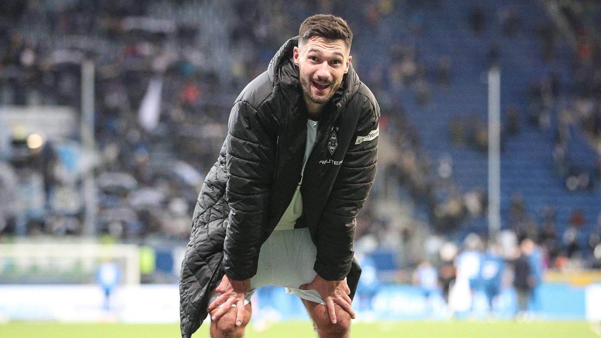 Borussia Mönchengladbachs Stürmer Tim Kleindienst steht nach dem Spiel bei der TSG Hoffenheim gebückt auf dem Platz und lächelt in die Kamera.