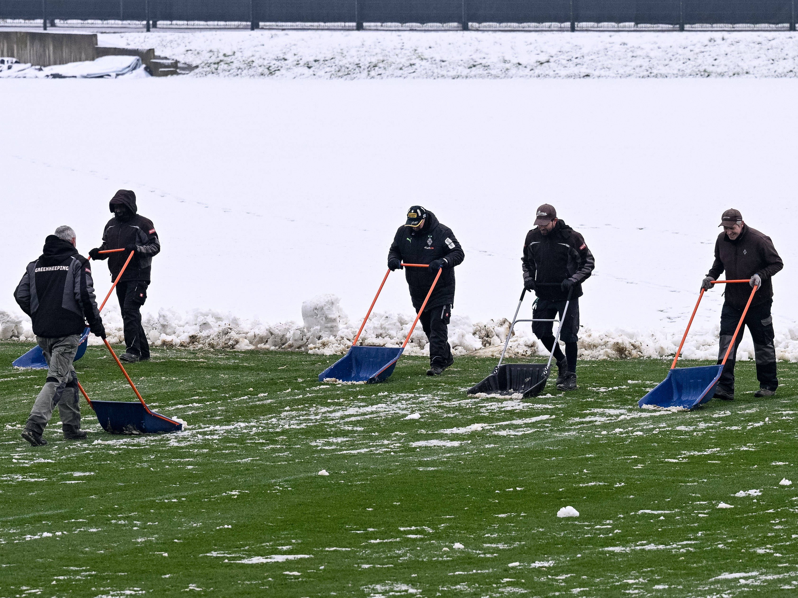 Helfer räumen mit Schneeschiebern den Schnee vom Trainingsplatz von Borussia Mönchengladbach.