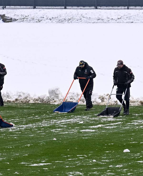 Helfer räumen mit Schneeschiebern den Schnee vom Trainingsplatz von Borussia Mönchengladbach.