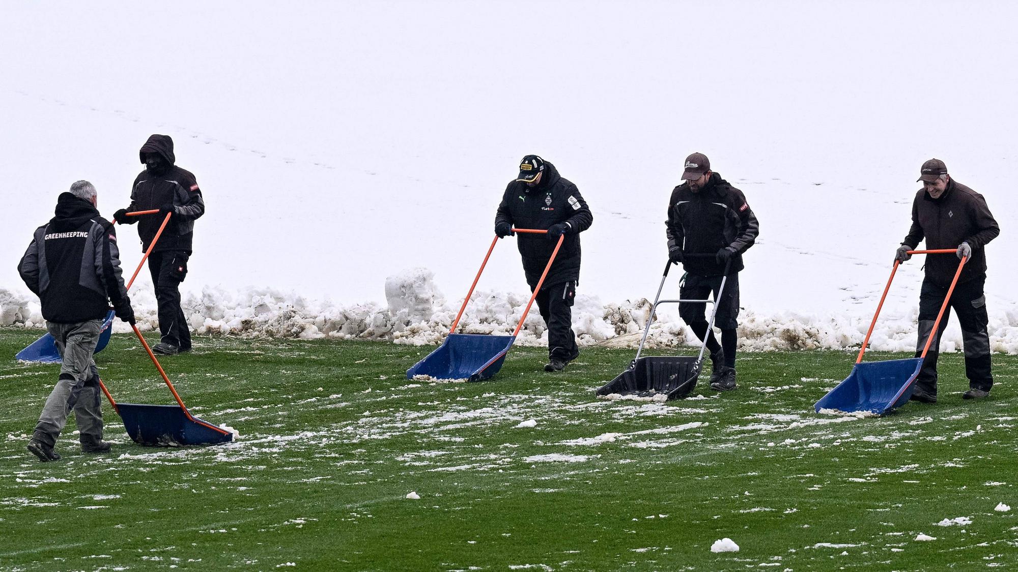 Helfer räumen mit Schneeschiebern den Schnee vom Trainingsplatz von Borussia Mönchengladbach.