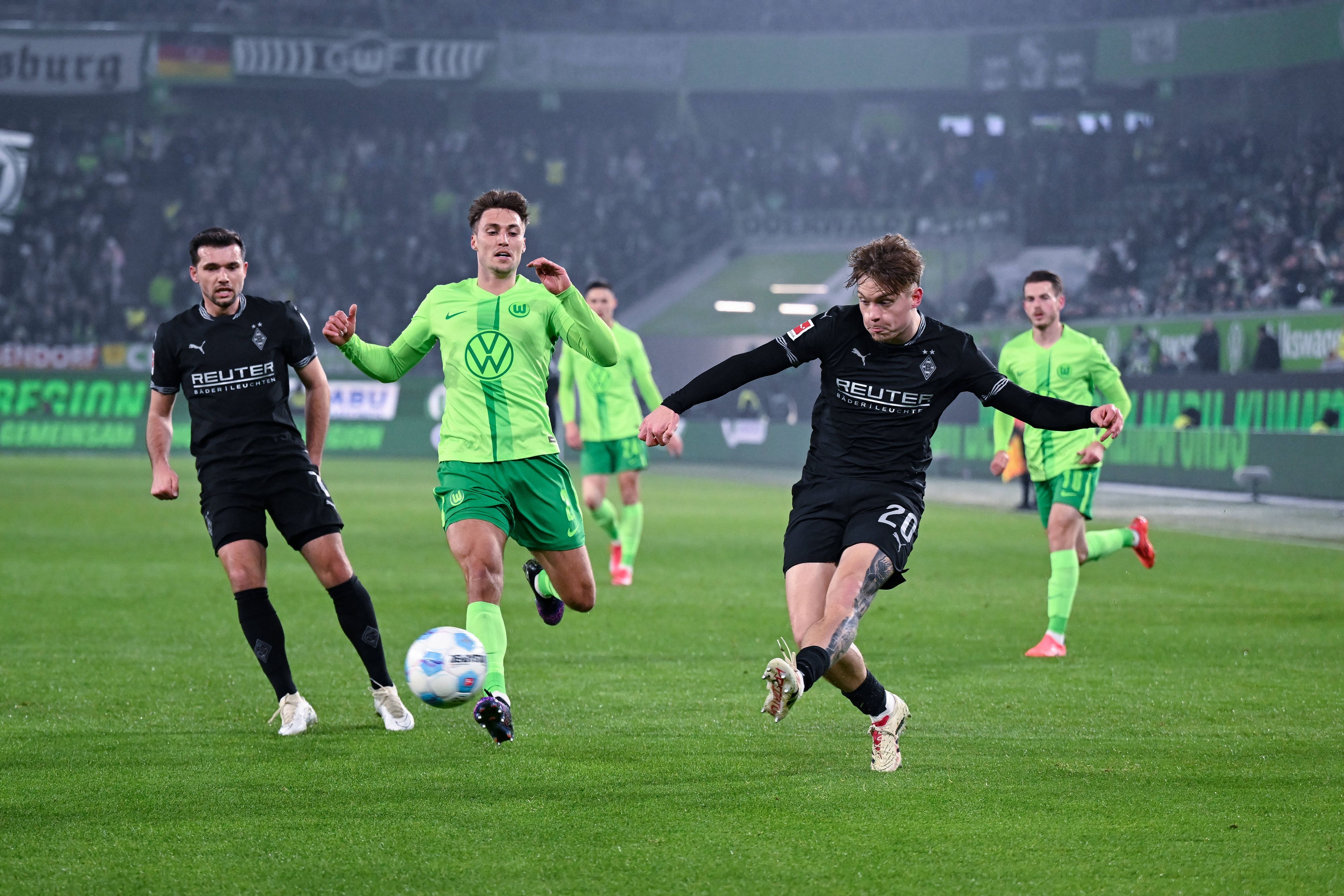 Borussia Mönchengladbachs Luca Netz schließt ab, Wolfsburgs Kilian Fischer kommt zu spät. Gladbachs Kevin Stöger beobachtet die Szene im Hintergrund.