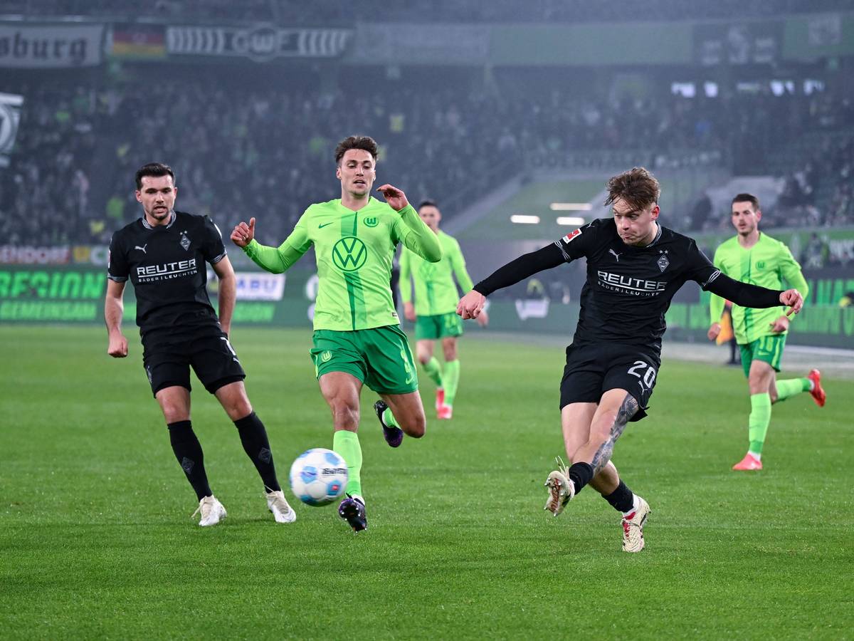 Borussia Mönchengladbachs Luca Netz schließt ab, Wolfsburgs Kilian Fischer kommt zu spät. Gladbachs Kevin Stöger beobachtet die Szene im Hintergrund.