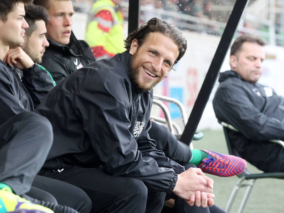 Preußen Münsters Jens Truckenbrod sitzt auf der Auswechselbank und lächelt in die Kamera.