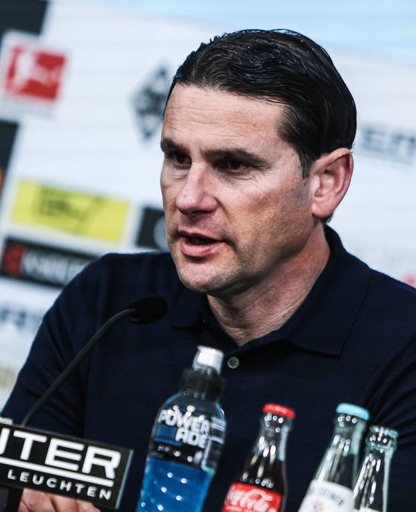 Borussia Mönchengladbachs Trainer sitzt bei der Pressekonferenz auf dem Podium und spricht ins Mikrofon.