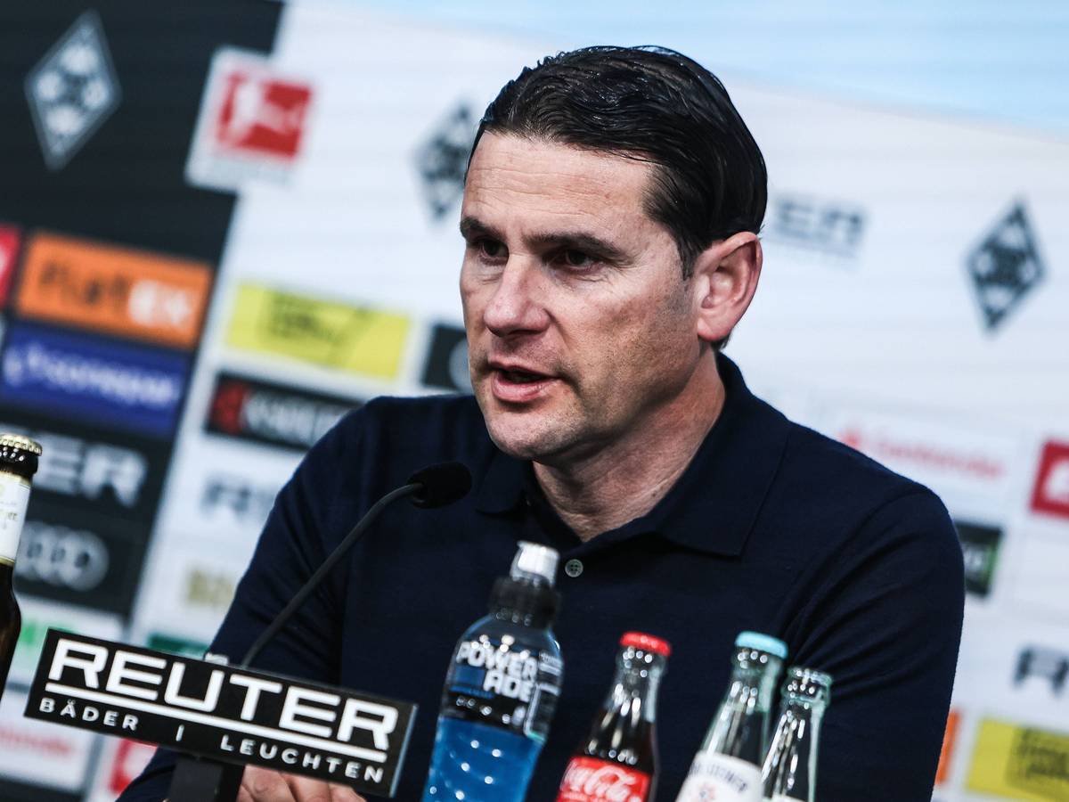 Borussia Mönchengladbachs Trainer sitzt bei der Pressekonferenz auf dem Podium und spricht ins Mikrofon.