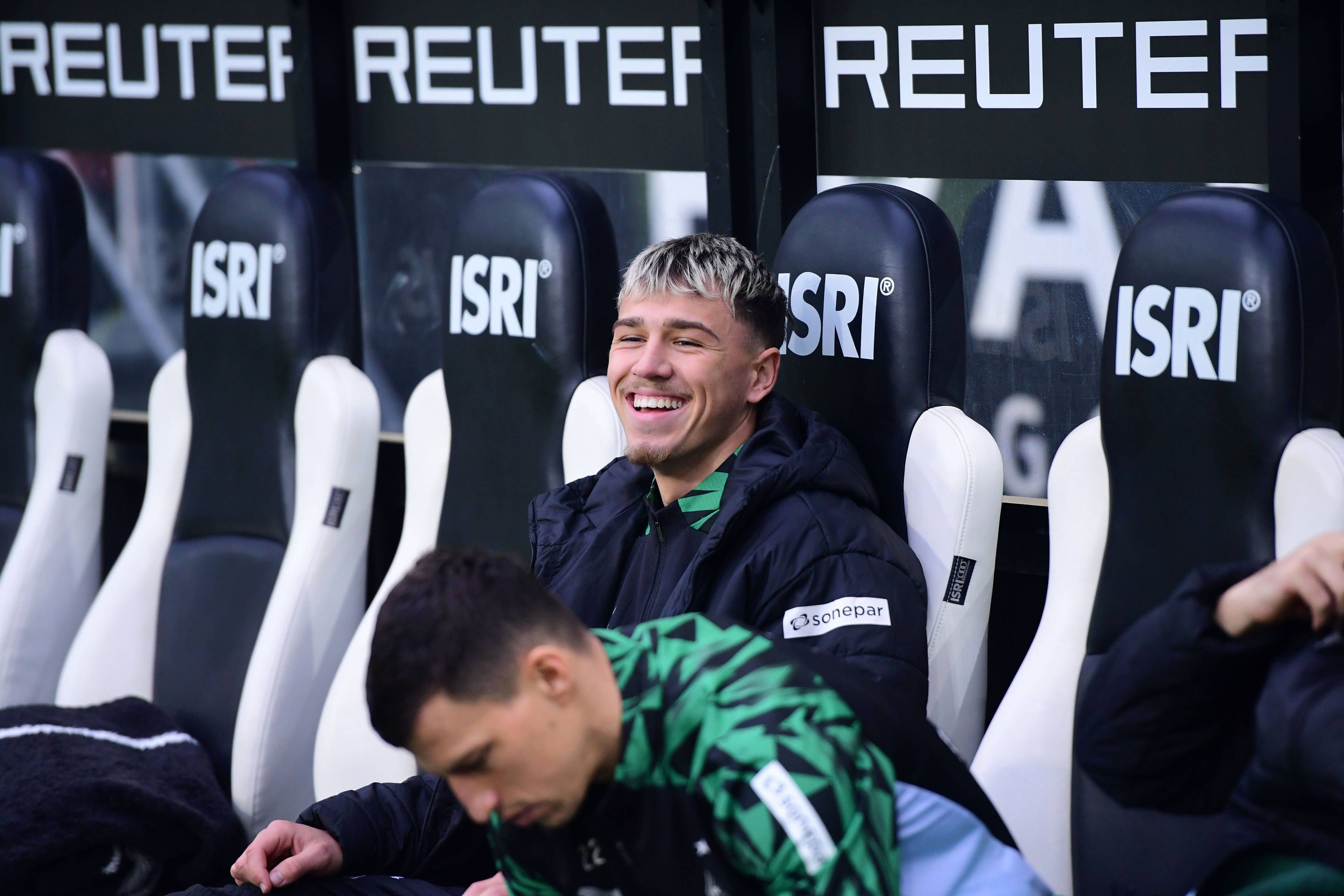 Borussia Mönchengladbachs Noah Pesch sitzt beim Bundesliga-Heimspiel gegen Holstein Kiel lachend auf der Ersatzbank.