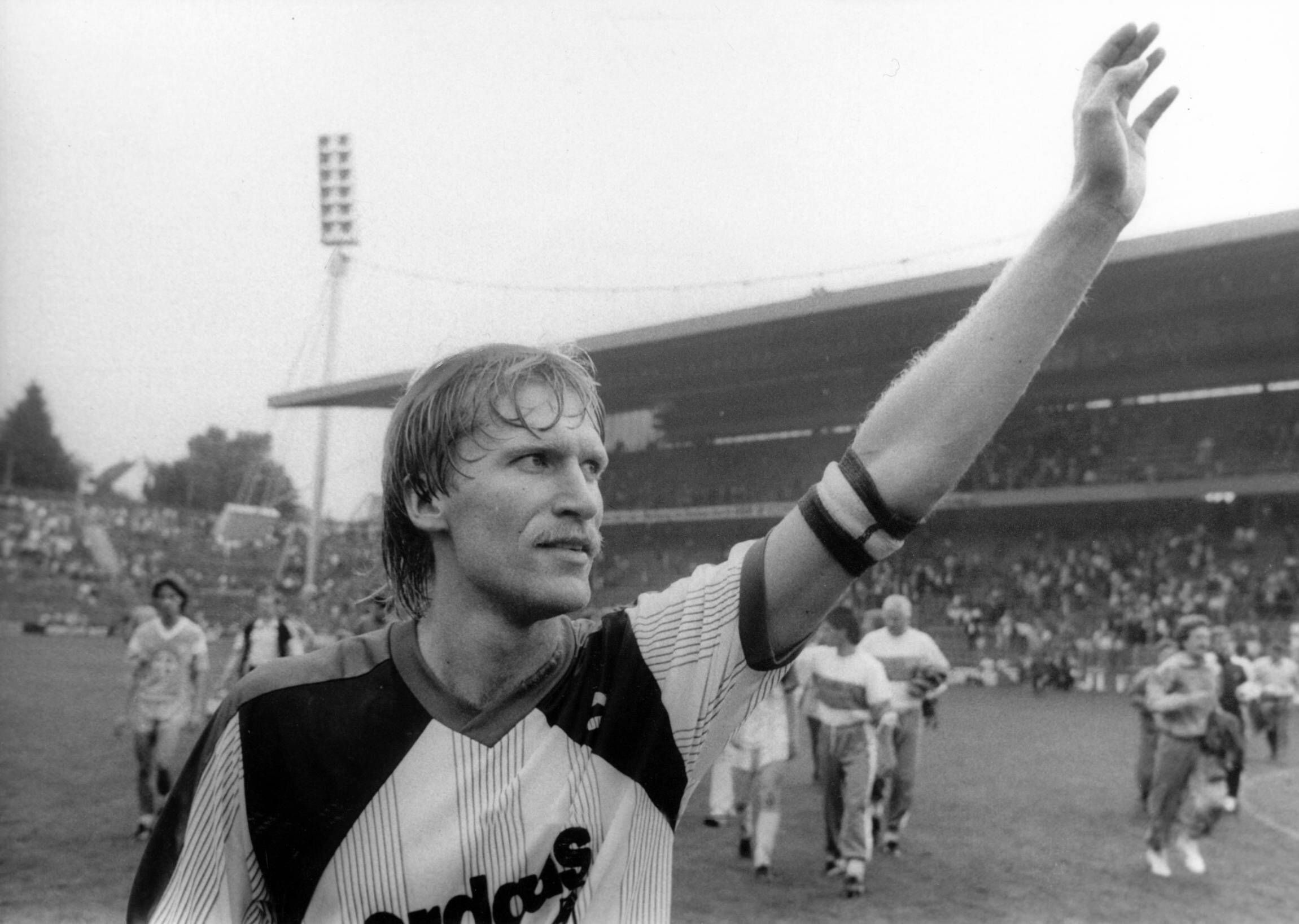 Uwe Rahn winkt mit der Kapitänsbinde am Arm.
