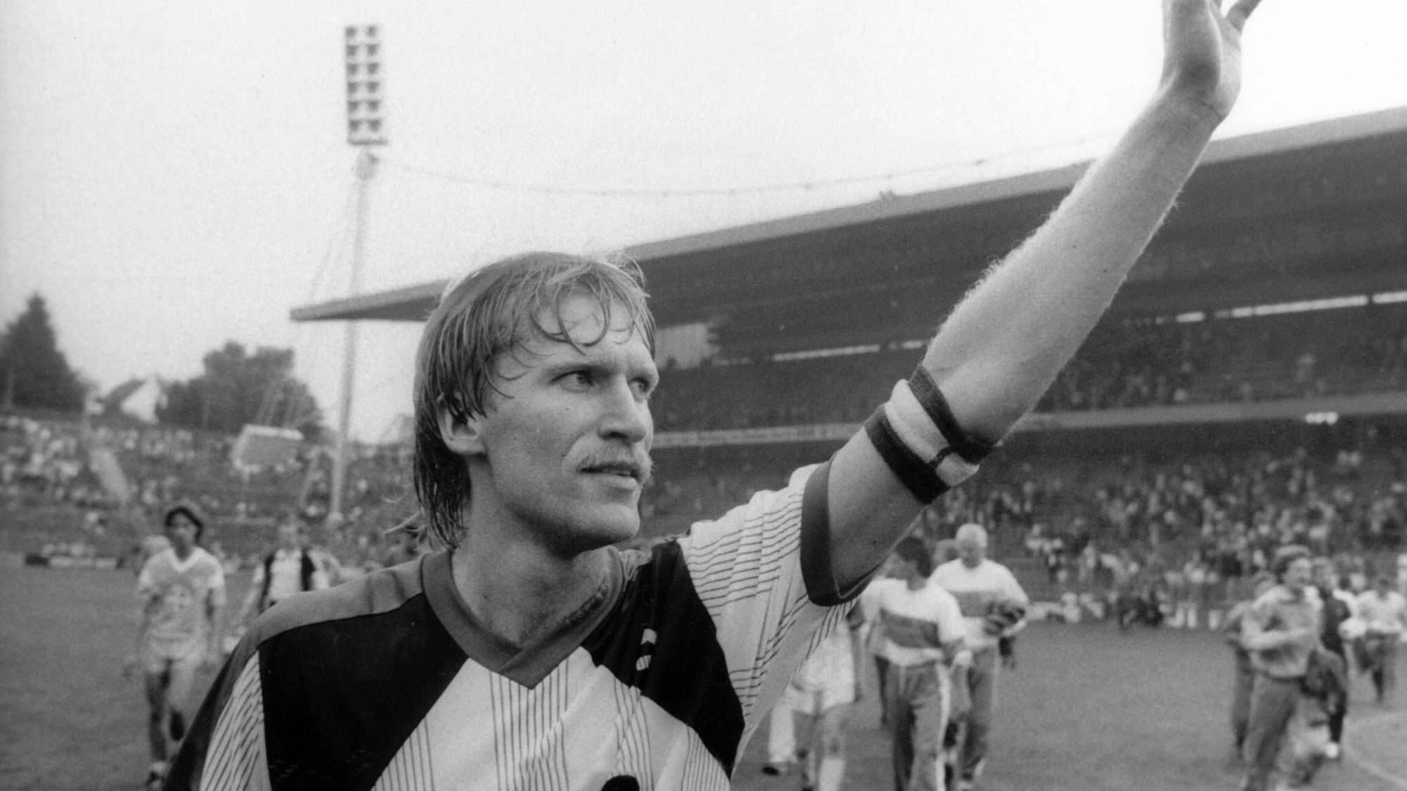 Uwe Rahn winkt mit der Kapitänsbinde am Arm.